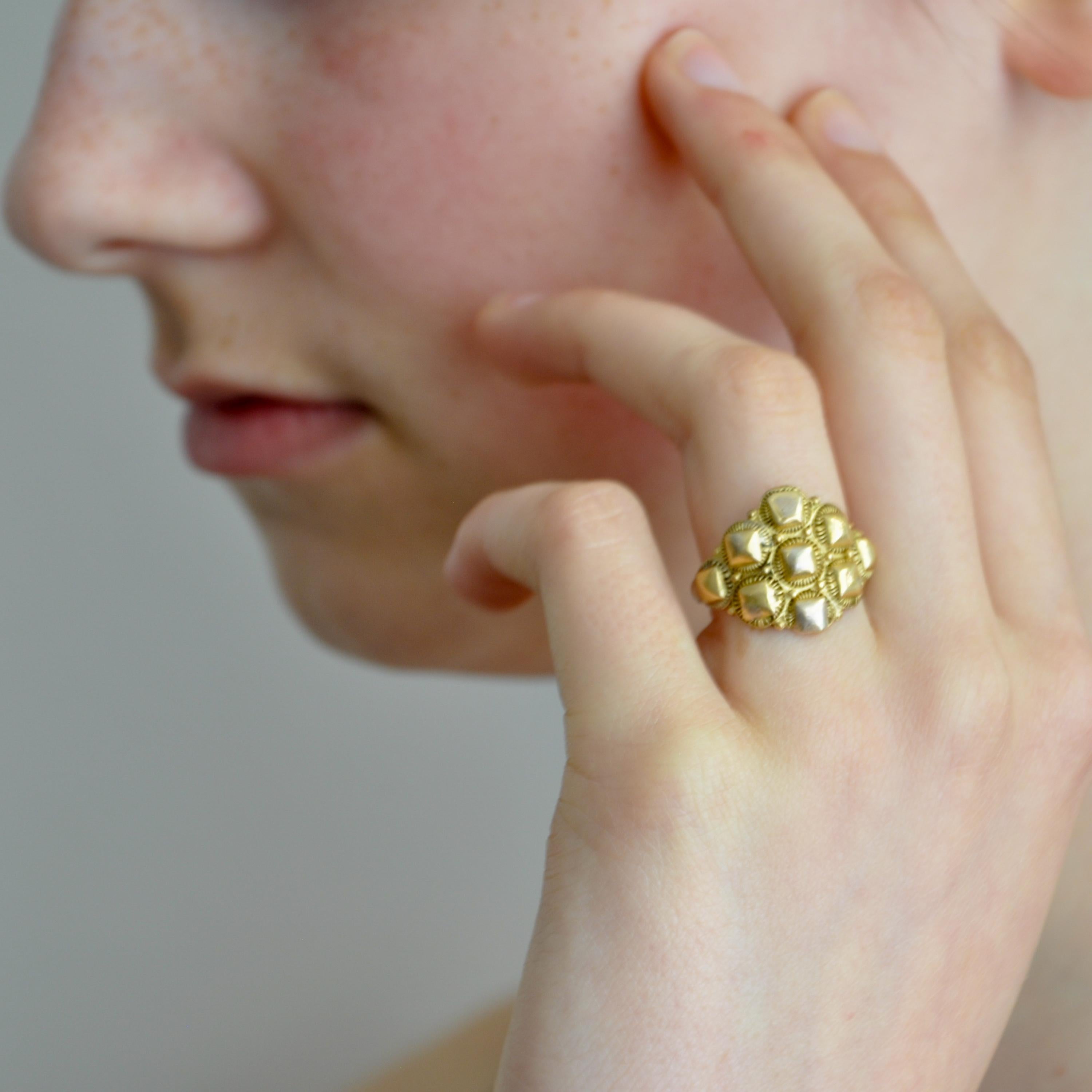 An antique baroque-style 14 karat yellow gold fantasy ring. The ring features an embossed design with small blocks. The rosette-shaped ring has nine gold faceted caps set within a spiral wire. These type of rings are in Dutch called 'prikkelring'.