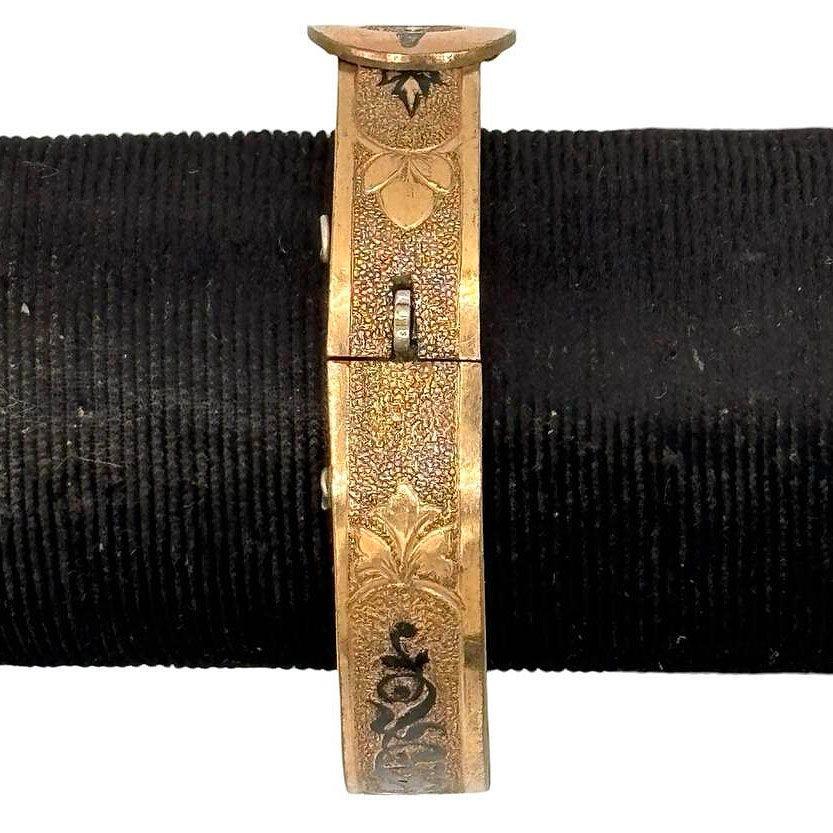 Late Victorian B&B Taille d'epargné S style gold-filled hinged bangle bracelet features an ornate belt buckle design adorned with intricate black enamel accents. The bracelet's detailed craftsmanship reflects the Victorian era's fascination with