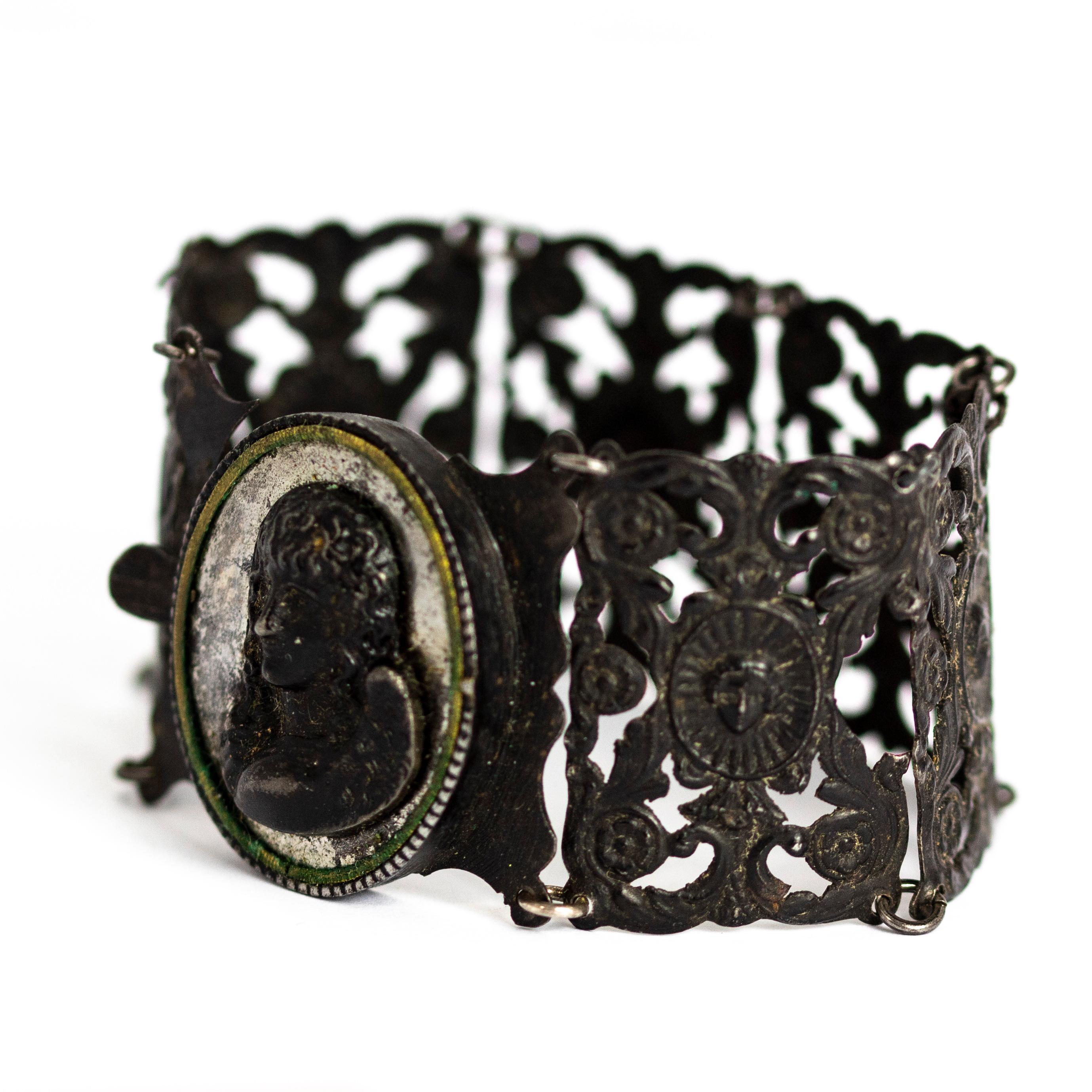 This intricate Victorian cuff bracelet is made of Berlin iron work. It is made up of 7 finely cast panels with flower and small detailed portraits, one of which has a large portrait of an angel held in an ornate oval frame. 

Length: 7 inches