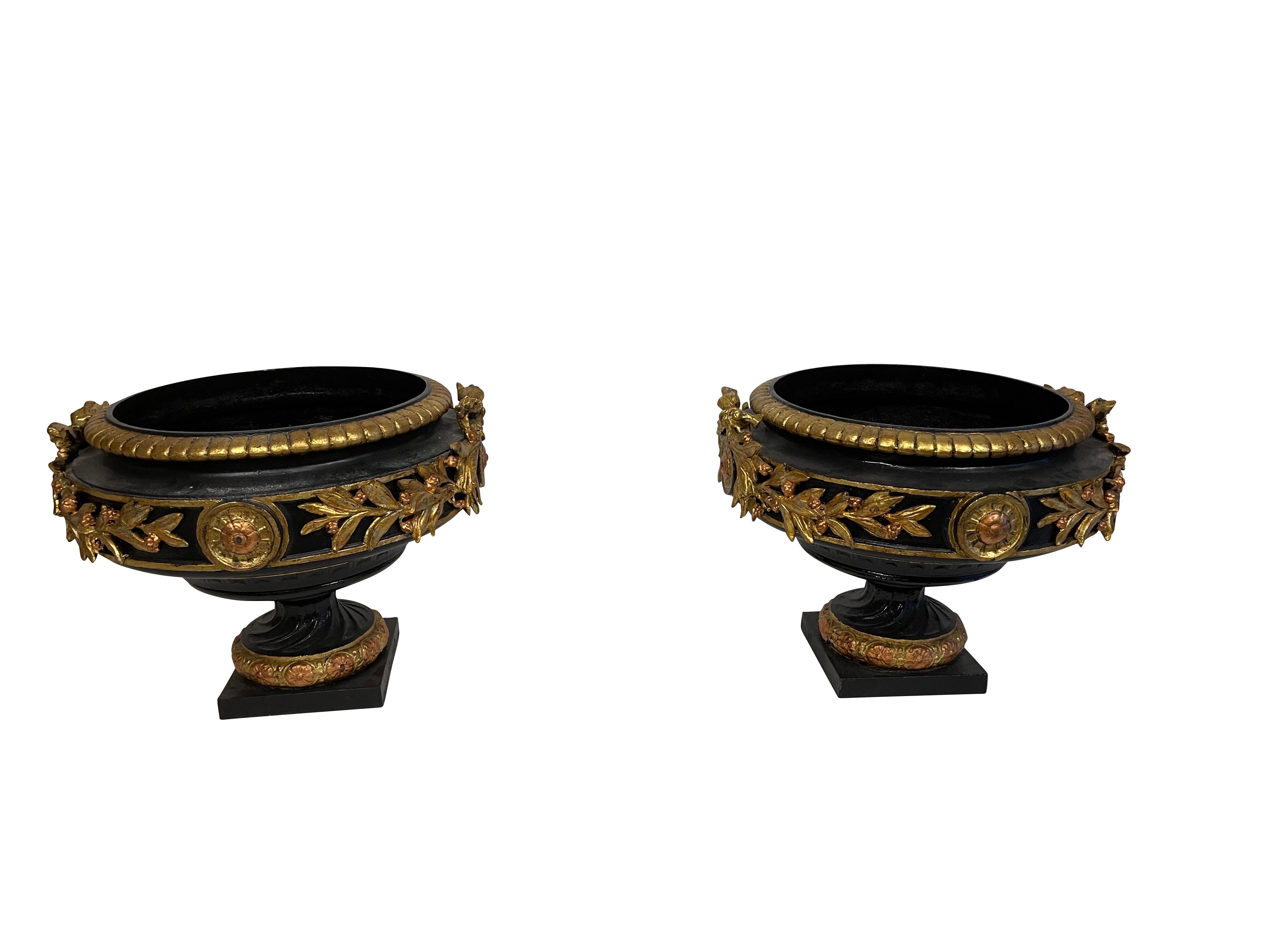 Pair of neoclassical black and gold classical cast iron urns. Spectacular pair with bow, garland and medallion decoration. Perfect to dress up a garden or indoors as planters.