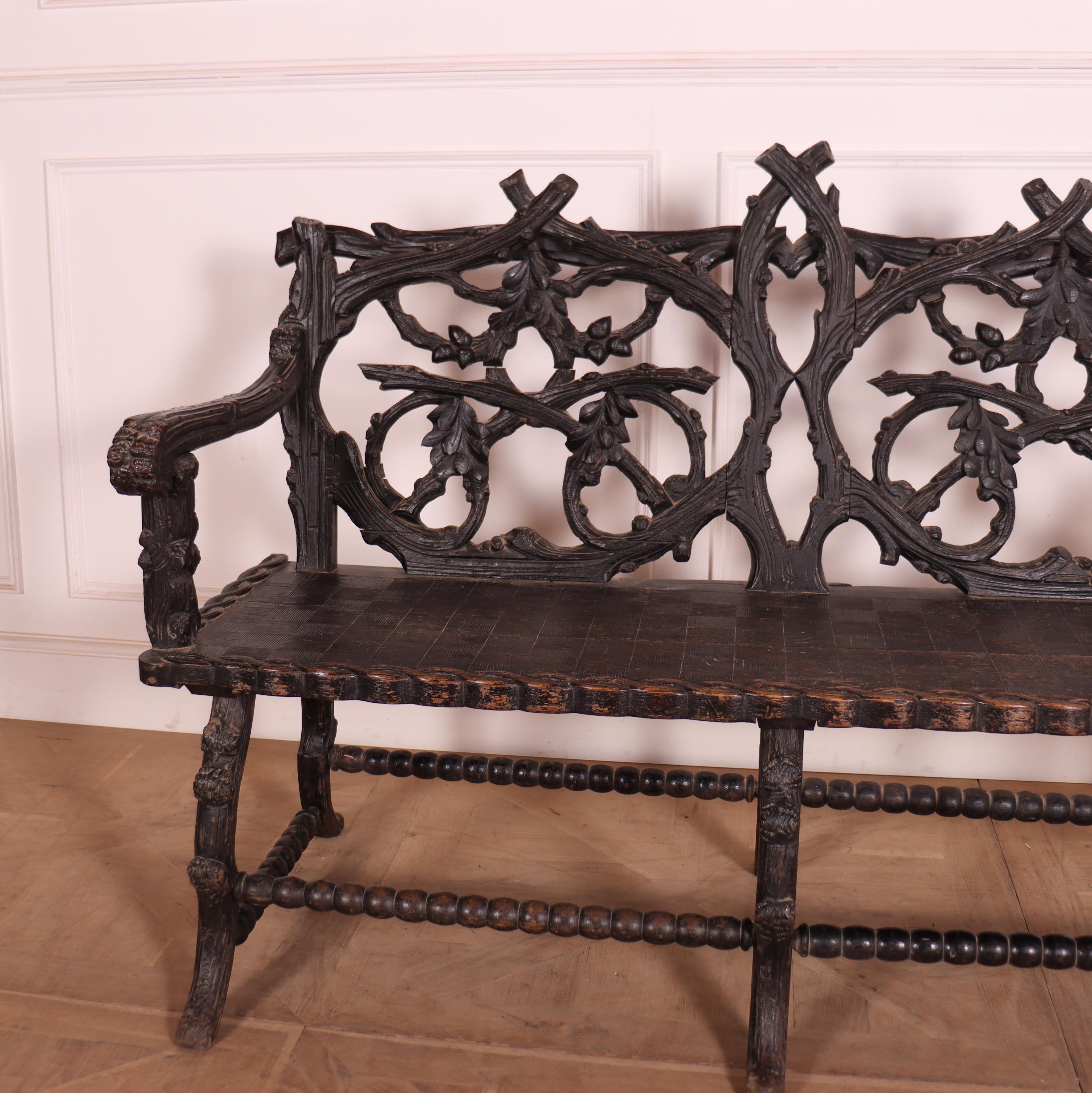 Victorian black forest carved bench seat. Back carved with branches, oak leaves and acorns. Patterned seat with scroll arms and entwined border. S scroll feet joined by bobbin turned stretchers. 1860.

Seat height is 19
