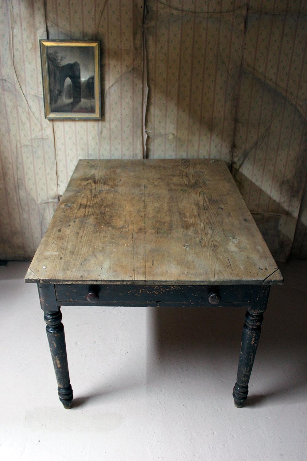The beautiful time worn painted pine farmhouse kitchen table, the original black paint distressed commensurate with age, having a four-plank top over two frieze drawers, one opening to reveal compartmentalisation for cutlery, the whole standing on