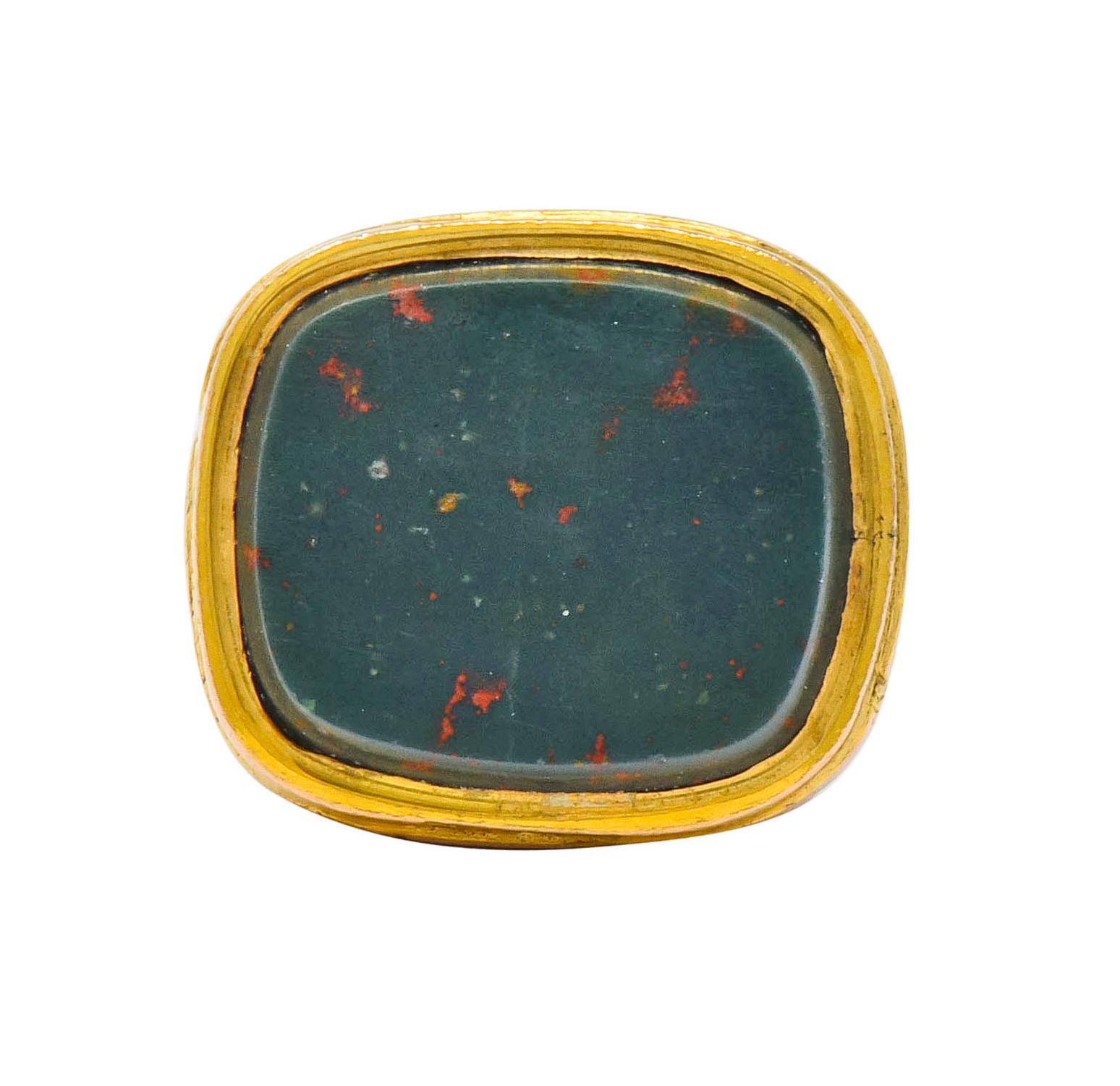 Fob designed with deeply engraved scrolled details and highly rendered dimensional forms

Bezel set with a cushion cut tablet of polished bloodstone; translucent and a very slightly bluish-green color with bright red flecks

Completed by jump ring