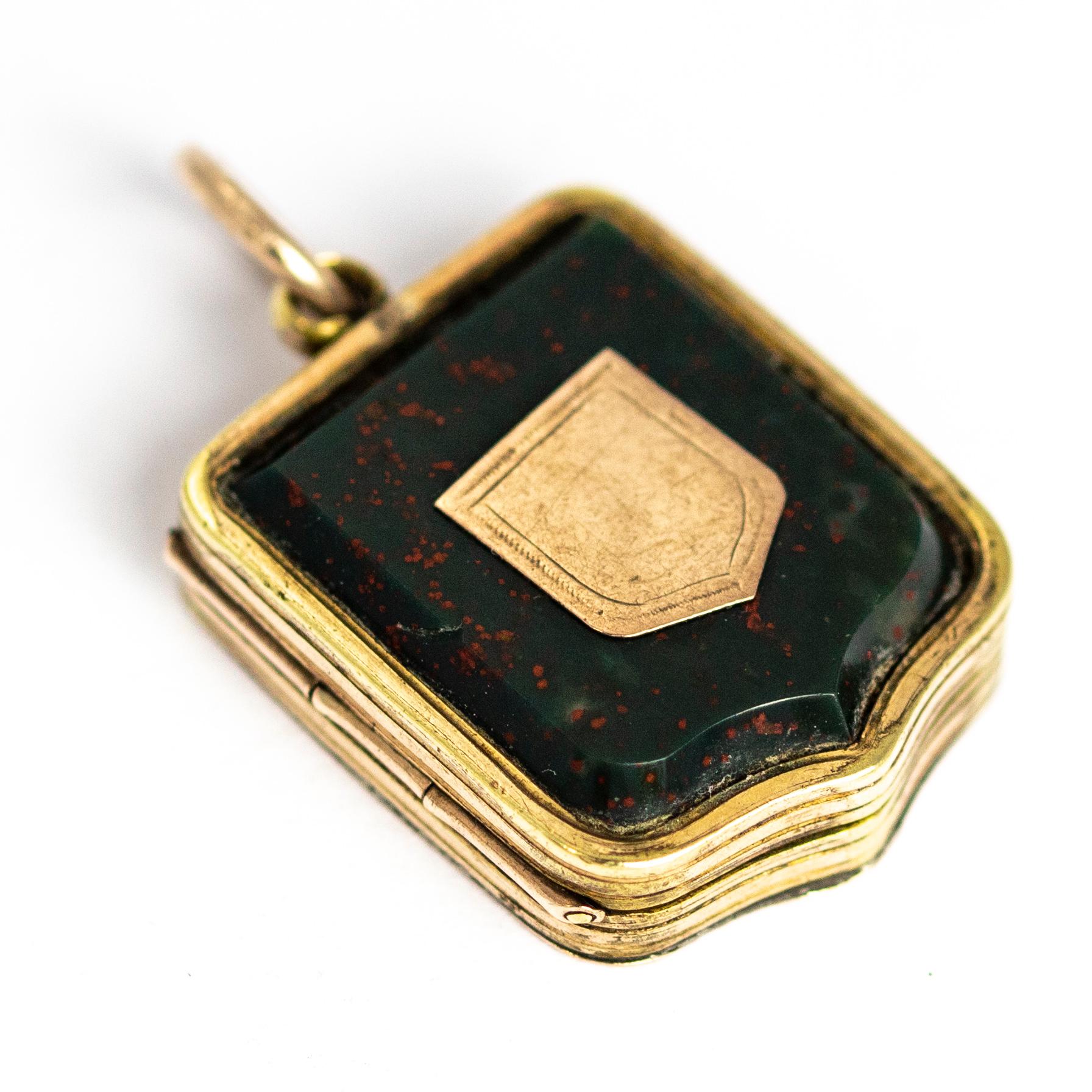 This unusual and wonderful locket has a glossy shield shaped bloodstone on the front of it with a gold shield placed in the centre. The back of the locket has intricate scroll and shield engraving. On the inside of the locket there is a picture of a