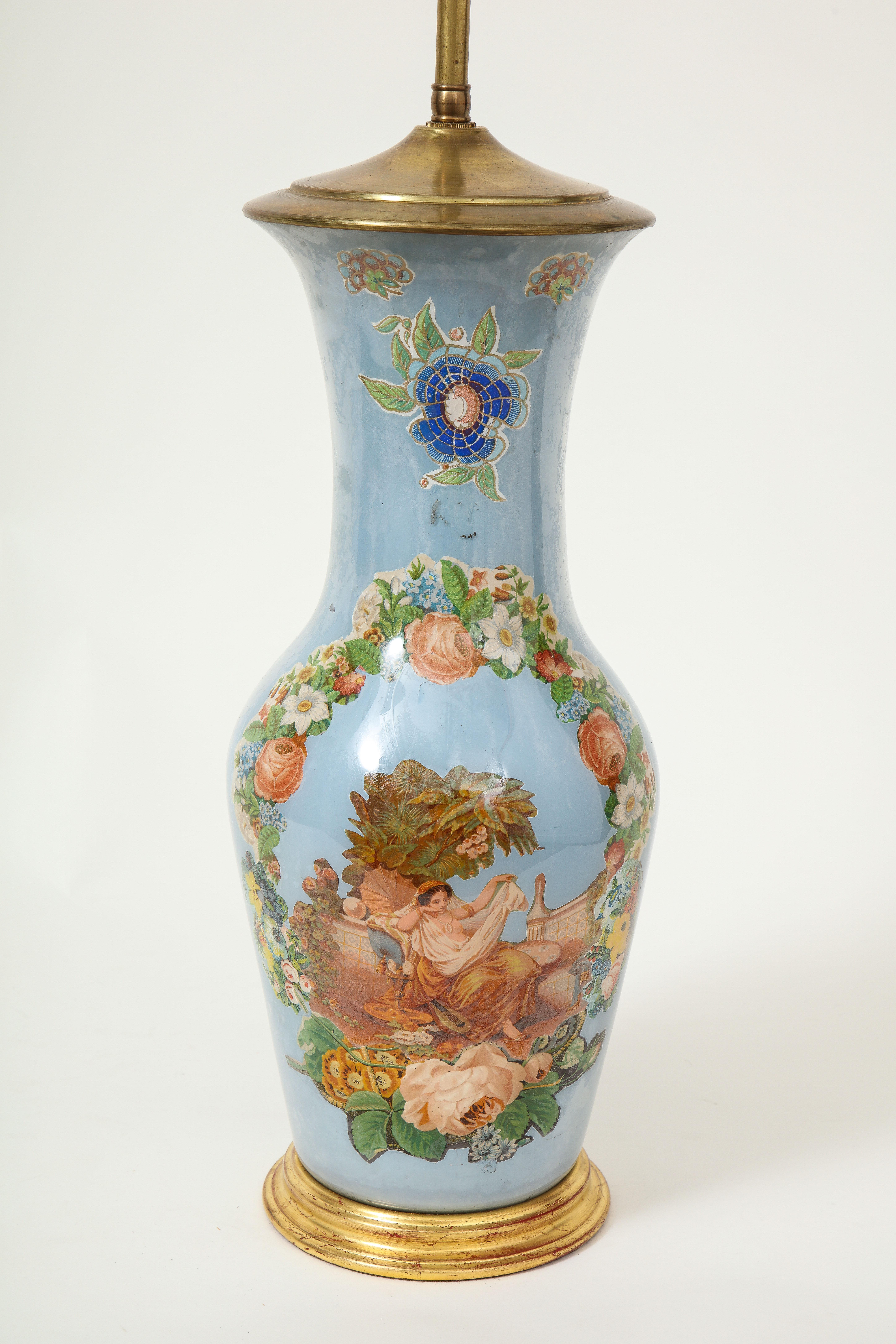 Featuring a floral wreath of roses, hydrangea, and daffodils encircling a classical maiden in deshabille, set below a morning glory, on a periwinkle ground; mounted on a turned giltwood base and fitted with a brass adjustable rod and two bulb