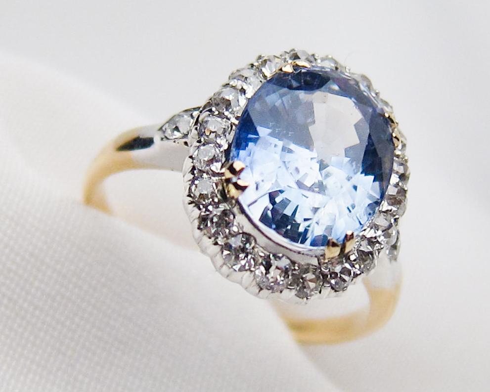 Circa 1880. This lovely sterling silver-topped 18KT gold Victorian ring features a gorgeous oval mixed-cut natural blue sapphire weighing 3.11 carats and set into a yellow gold four-split prong head. The sapphire is haloed with 20 round single-cut