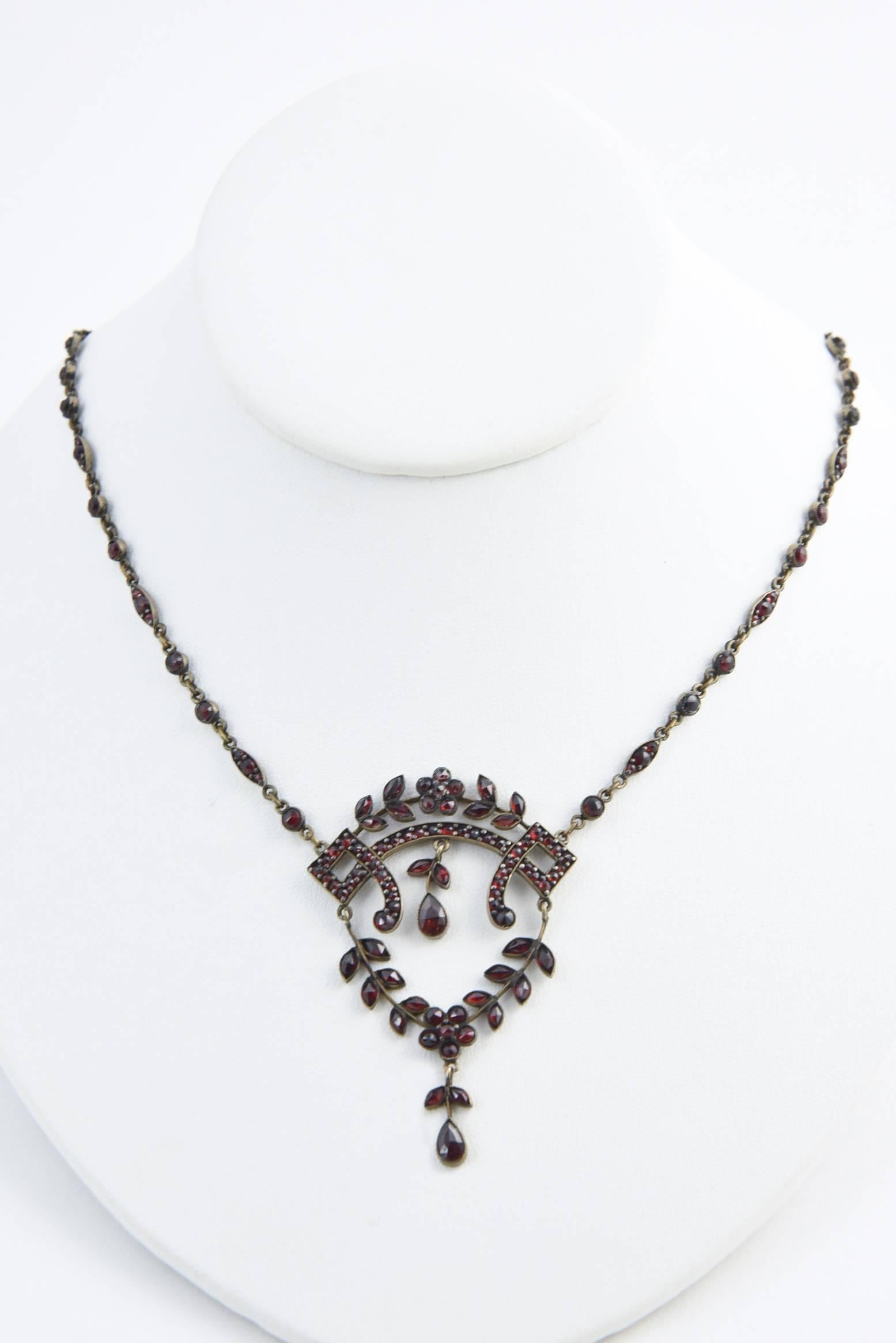 Victorian Bohemian garnet necklace centrally set with an open-frame pendant decorated in garland motifs. The pendant suspends from a sectional repeated design of links flanked with beaded spacers ending with a floral clasp