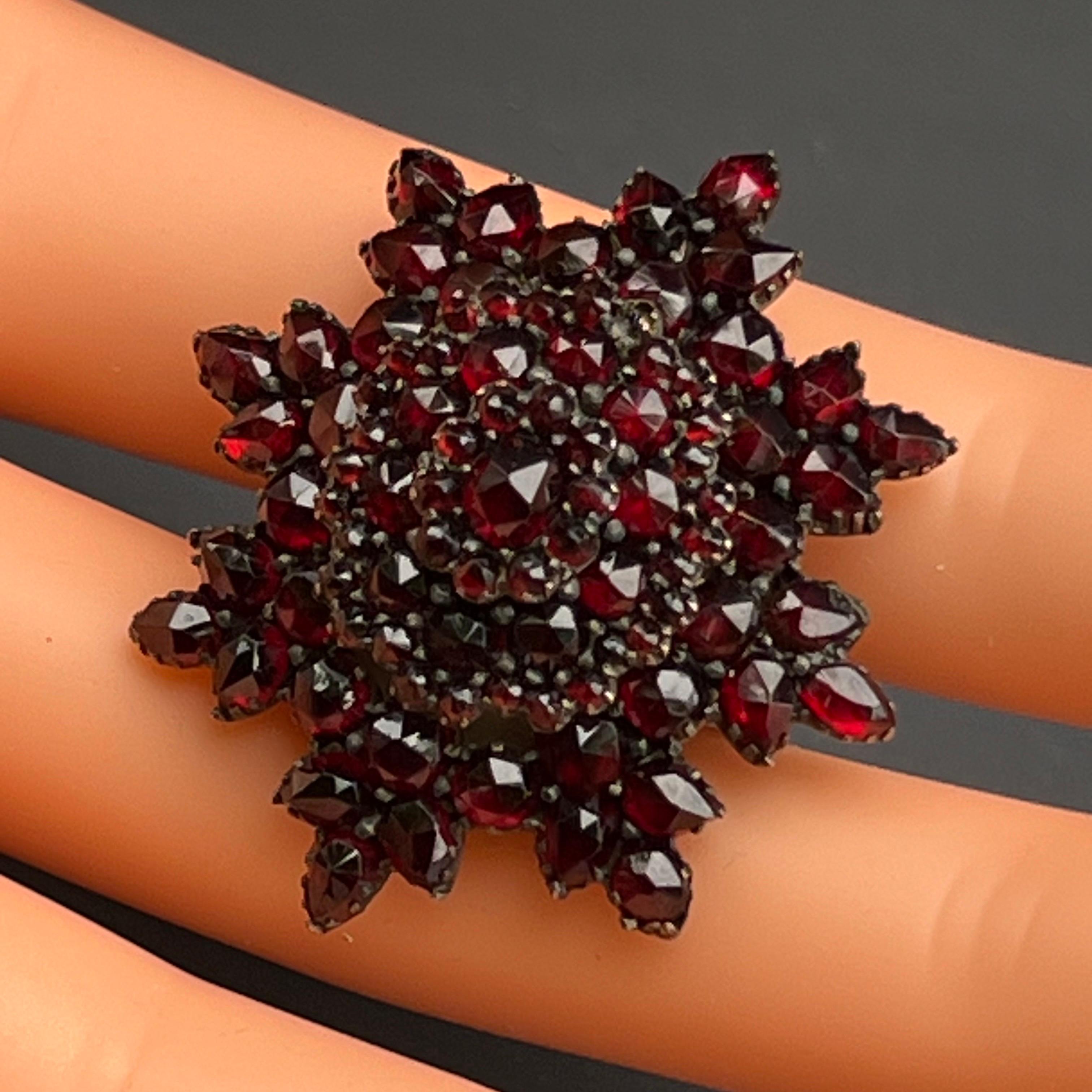 Questo squisito pezzo emana l'eleganza di un'epoca passata. Realizzato in argento dorato, presenta autentici granati di Boemia sfaccettati e tagliati a rosa meticolosamente incastonati su una cornice d'argento. Il design versatile funge da