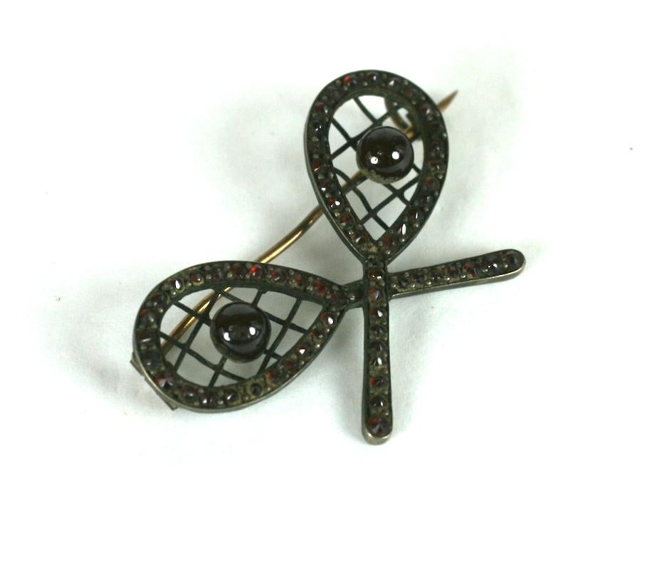 Charming Victorian bohemian garnet crossed tennis rackets brooch. Set in gold filled metal with fine wire cross hatching, garnet pave with garnet beads as the tennis balls. Sport motif brooches were often prizes given at sports tournaments and