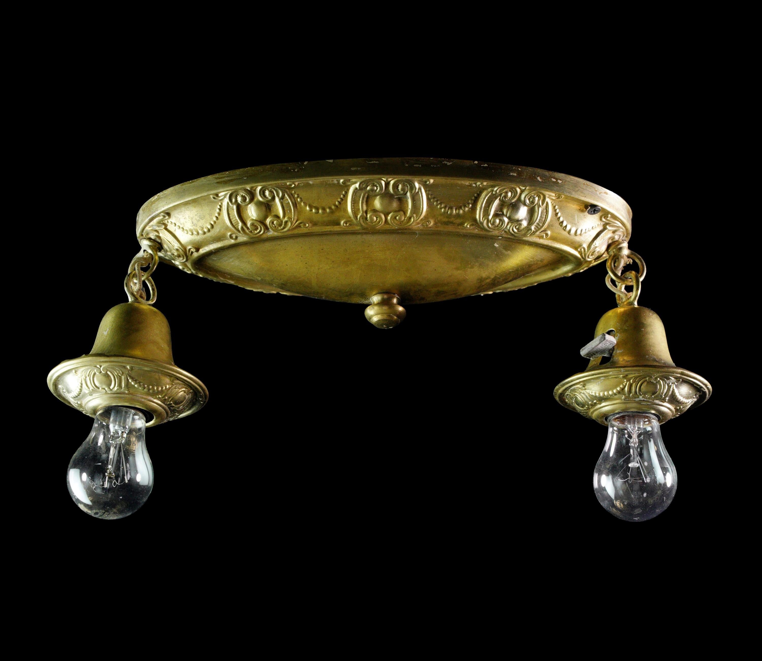 Enhance your space with the elegance of our antique early 1900s brass two light flush mount fixture with two exposed bulbs. The light features an oval canopy with Victorian detailing in the form of scrolling and beading and two downward facing