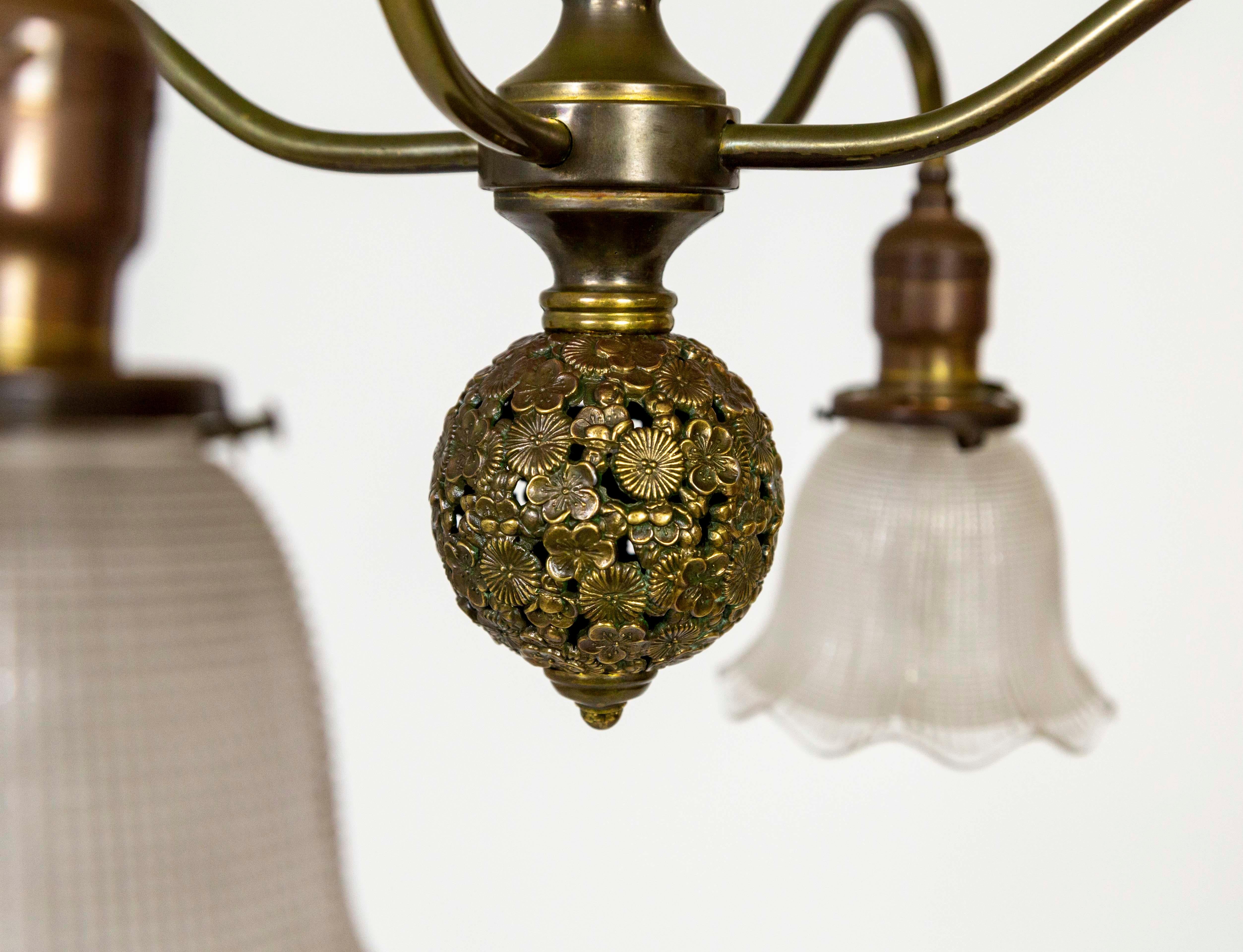An Aesthetic, Victorian, 4-light chandelier with bellflower-shaped, holophane glass shades. The curving, brass arms extend from one of four decorative spheres off the stem. The bottom ball has a beautiful texture, it is composed of small cast