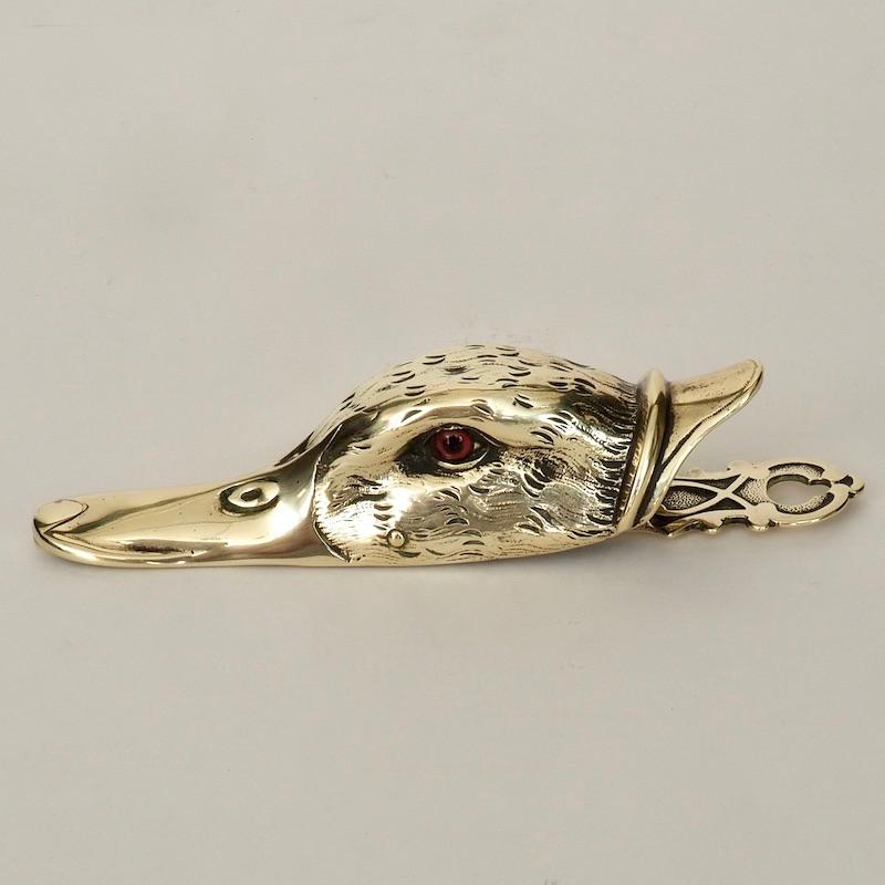 A Victorian duck's head brass letter clip, set with red glass eyes. The duck's beak is sprung in order to hold letters or memos and can be wall hung through a mounting hole to the rear. Well crafted and useful novelties such as these typical of the