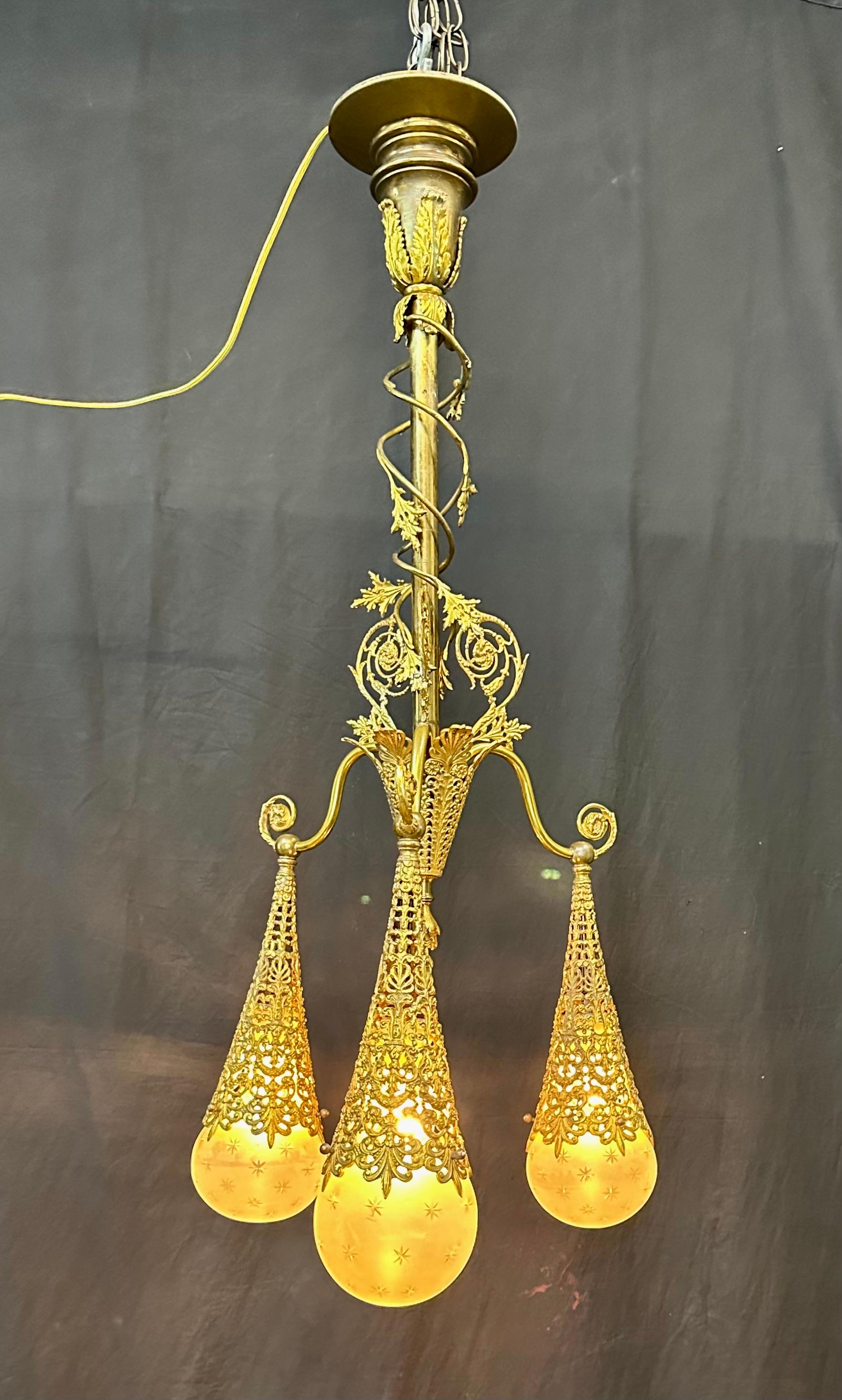 Questa elegante plafoniera vittoriana in ottone è progettata con un elaborato motivo di filigrana scolpita. Tre bracci arricciati, ciascuno dei quali termina con un cono decorativo in ottone filigranato, sono sospesi a un gambo decorativo. Ciascuno