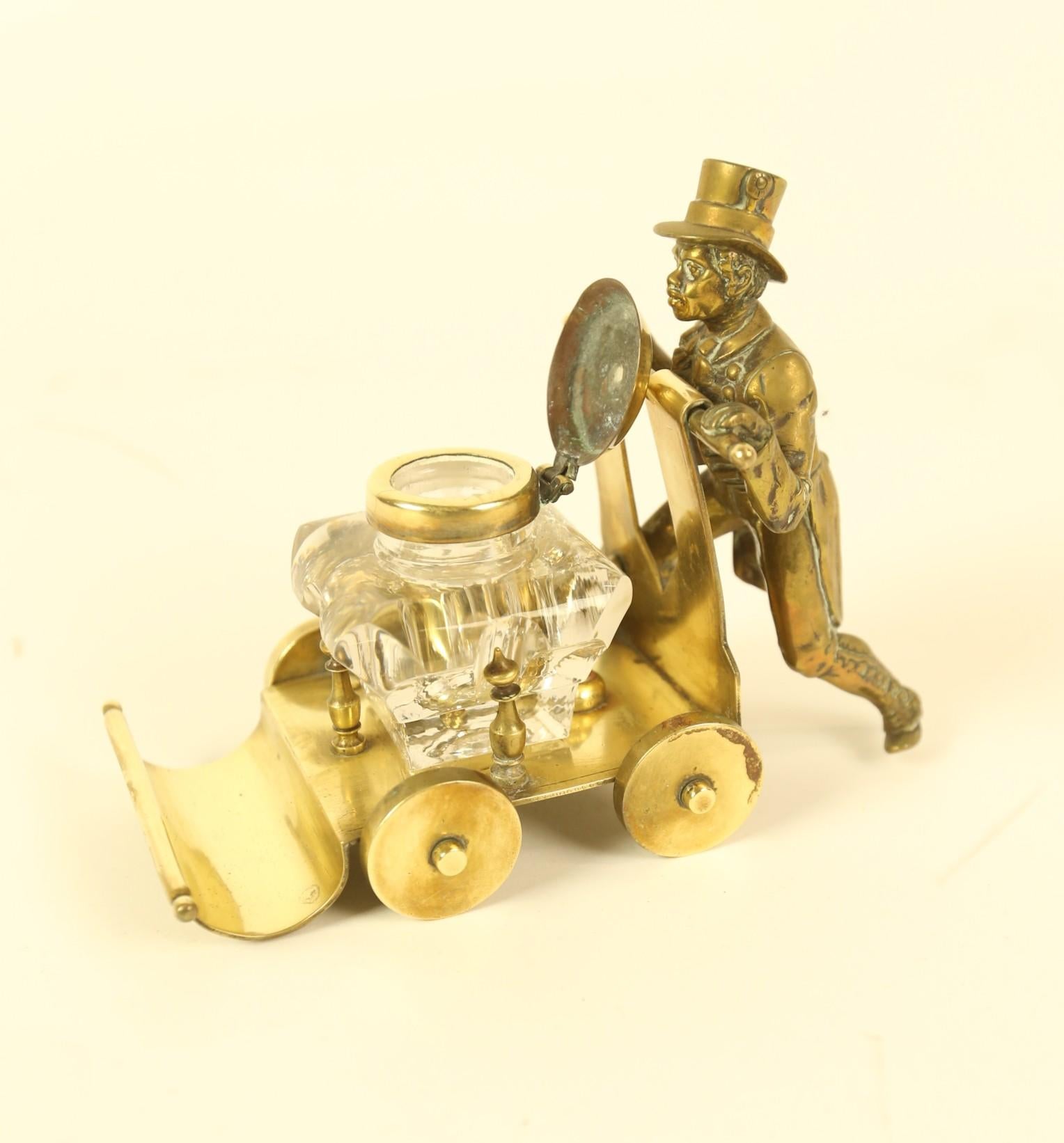 Victorian Brass ink stand  in the form of a  Gentleman Pushing a cart 
Cast Brass Figure of a gentleman with a top hat 
Brass cart
Pen stand in front, 
Moulded glass inkwell with brass lid
4 moveable wheels on cart
Recent polish
Good detailed Casting