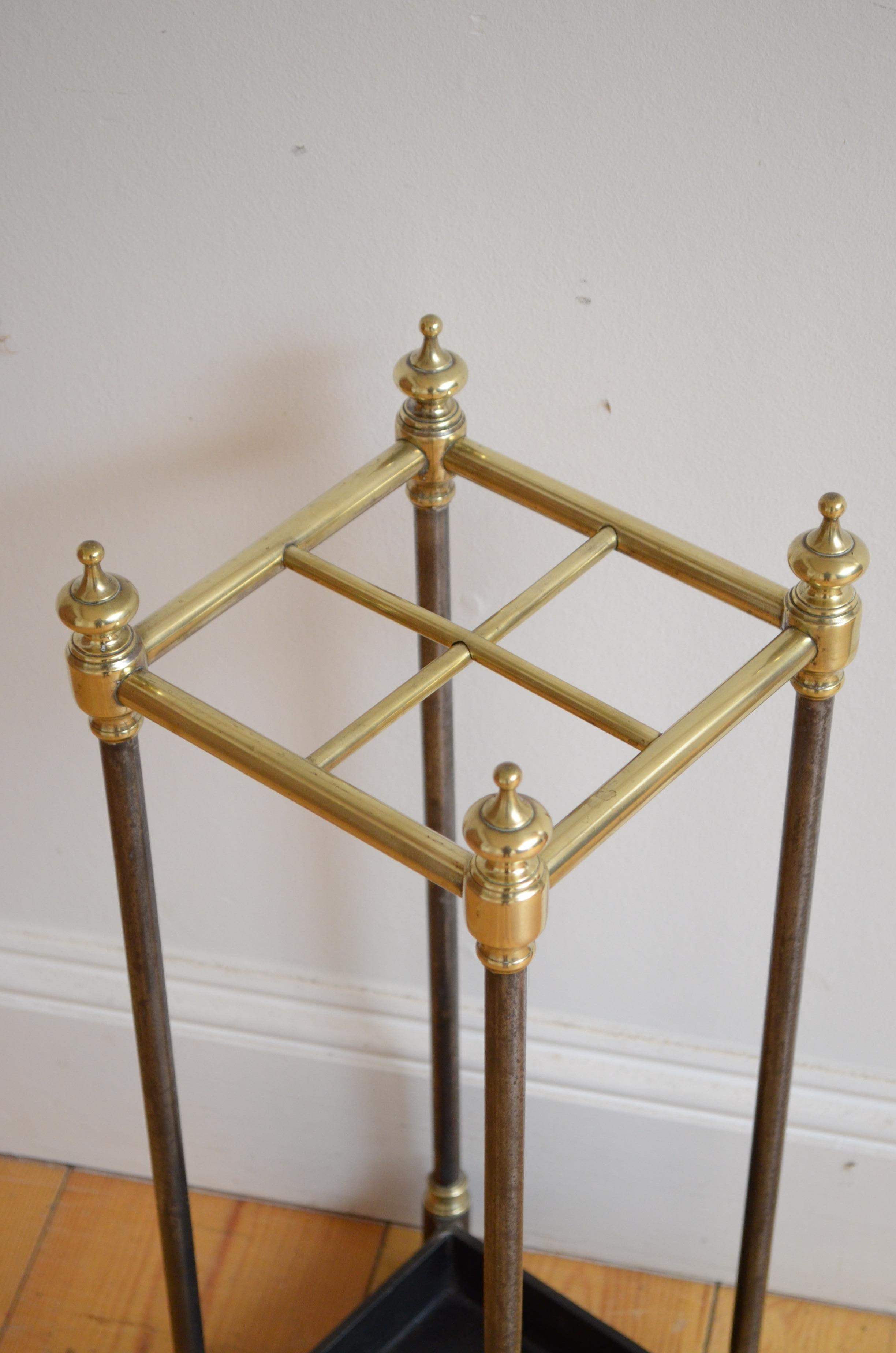 K0215 English Victorian brass umbrella stand with four compartments, decorative brass finials, steel uprights and cast iron base. This antique umbrella stand has been syamthetically cleaned and polished and it is in home ready condition.