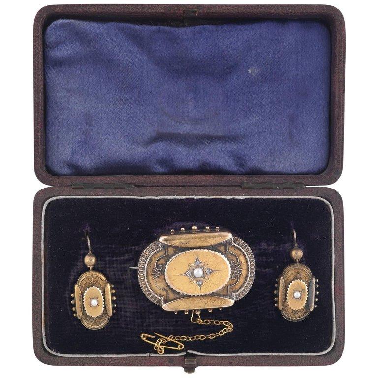 Composed by the an half pearl brooch centered cartouche shape brooch with at the back the inscription dated 1884, presented by Mrs. Kennedy for her husband's retiring;
the two earrings of similar design with sheperd's hook back.

Mounted in yellow