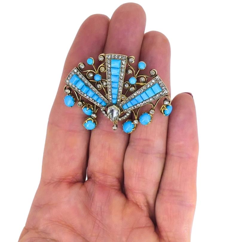 Charmante broche victorienne en or 18 carats, ornée d'une turquoise et d'un diamant.
La forme en éventail de la broche est ornée d'une combinaison de pierres de turquoise taillées en cabochon de différentes coupes, telles que ronde, ovale et