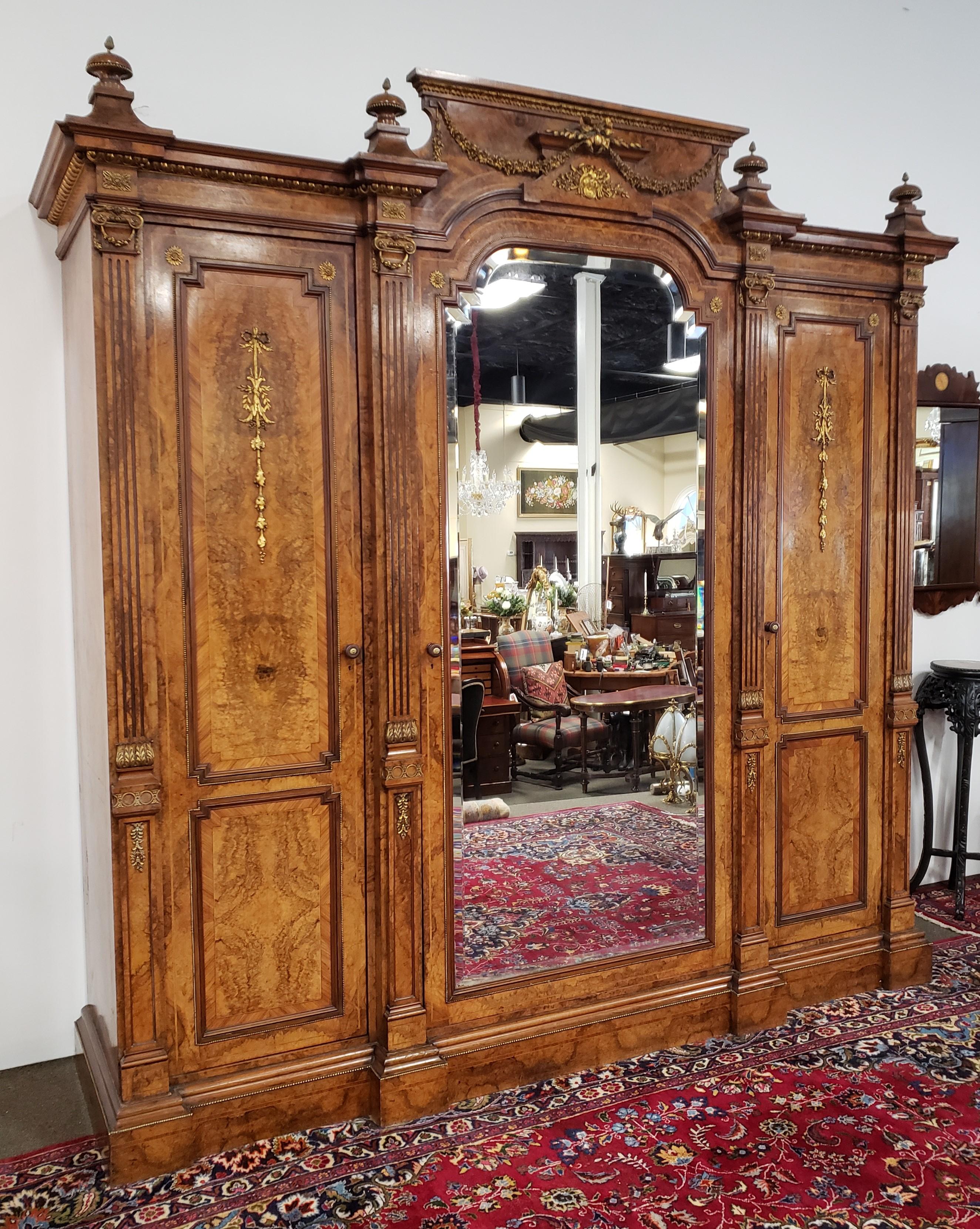 Victorian burl walnut armoire with crossbanding and satin wood inlay. This piece features a large mirrored door in the center. When opened it reveals a linen press century displaying an interior with slide out trays and 3 drawers. The left and right