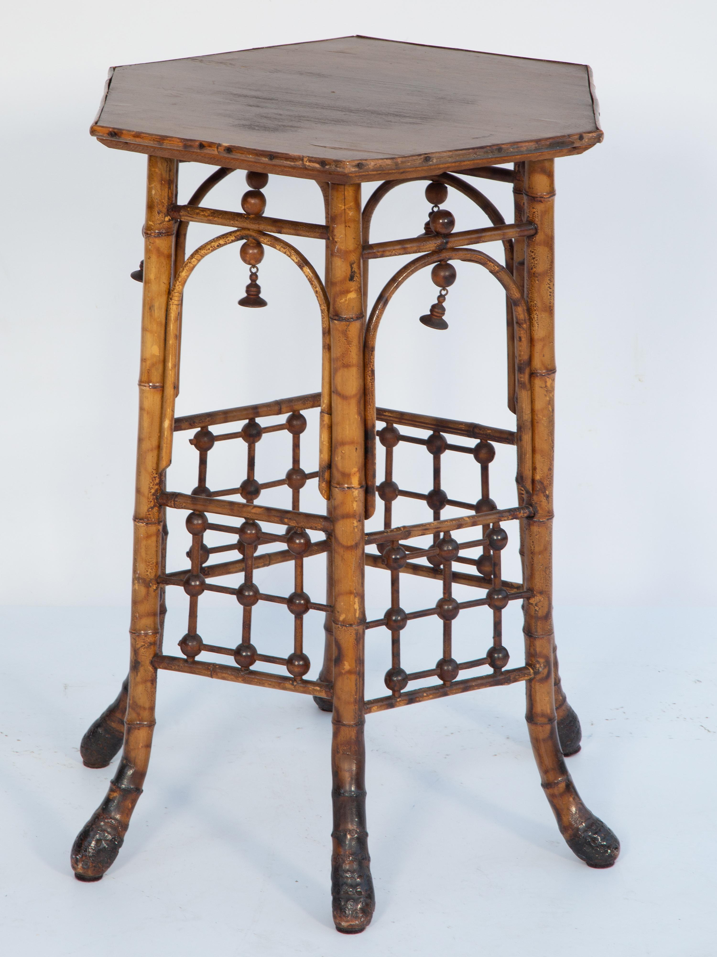 Victorian table, of burnt-bamboo, having a hexagonal top of wood, with carved bells hanging from its underside; set upon conforming stand of arches and fretwork, raised on splayed, bamboo-root feet.

Stock ID: D3857