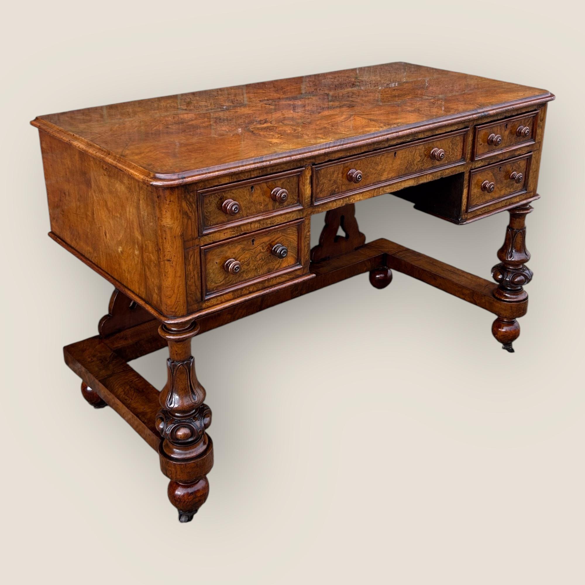Here we have an Antique Victorian (1837-1901) Burr Walnut Desk with a quarter veneered burr walnut top, carved front legs, 5 drawers, all with wooden knob handles and casters (wheels) on the bun feet.