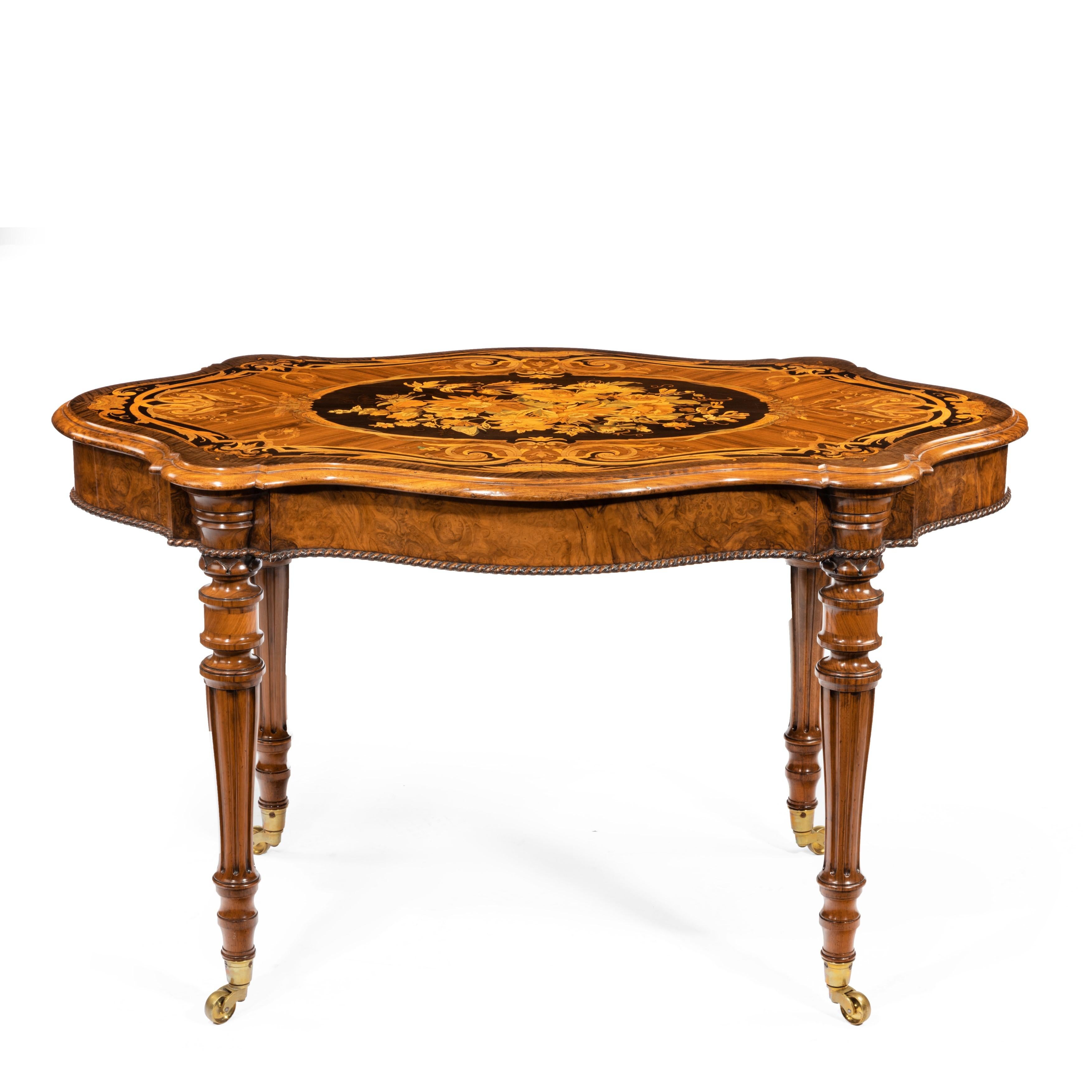 A Victorian burr walnut marquetry library table, the lobed top above a disguised frieze drawer raised upon four turned and fluted legs with kingwood banding, decorated with a large central oval inlaid with a bouquet of flowers with butterflies and