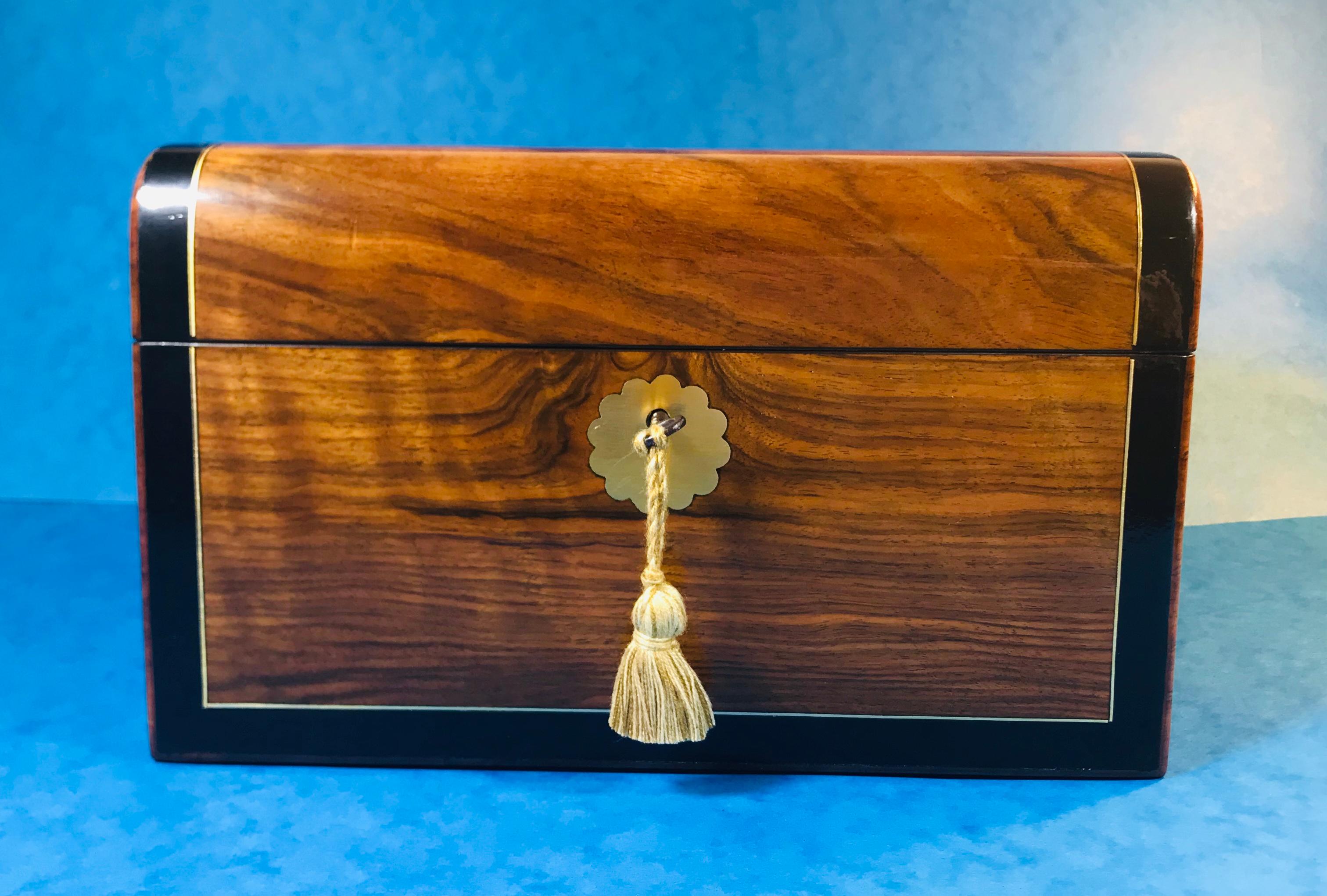 Victorian circa 1870 walnut jewelry box.
A beautiful jewelry box with a dome shaped top, inlaid with brass, ebony banded and crossbanded in Tulipwood. The box has a brass top and key escutcheon and a working lock and key. Open the box to reveal a