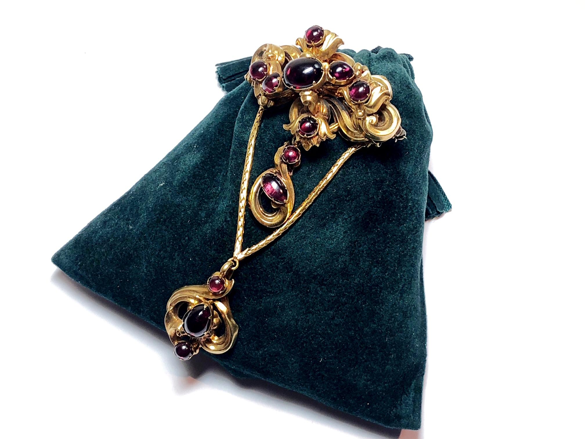 A Victorian garnet brooch, set with cabochon cut garnets set in a floral motif, suspending another cabochon garnet drop, with a further cabochon garnet drop suspended from two gold rope chains, circa 1875