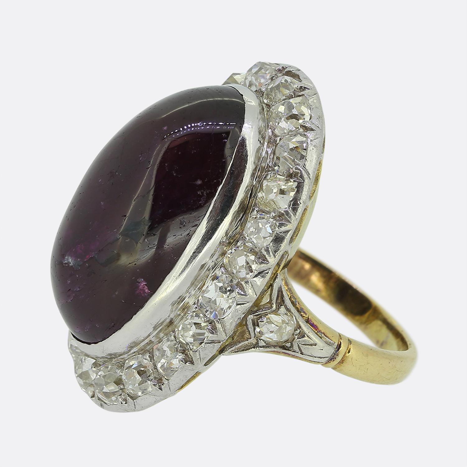 Here we have an impressive 18ct yellow gold ruby and diamond cluster ring. At the centre of the face we find a large oval cabochon ruby which is a dark red hue. The ruby is then surrounded by contrasting stunning bright white old cut diamonds that