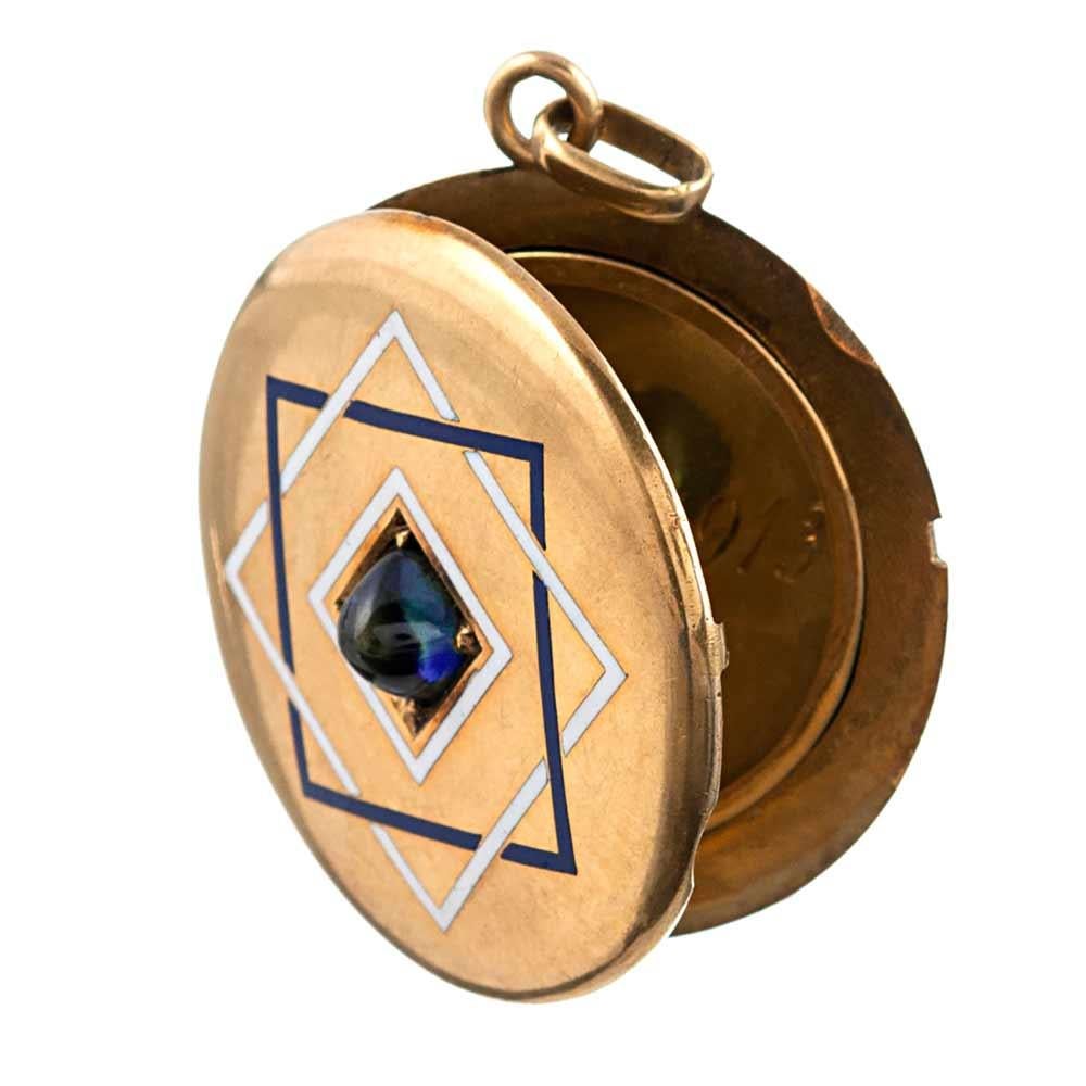 A perfectly round and mid-size 18k yellow gold locket displaying the complex beauty that is characteristic of late Victorian jewelry. The piece is decorated on the front with a sugar-loaf cabochon sapphire, set in the center of blue and white