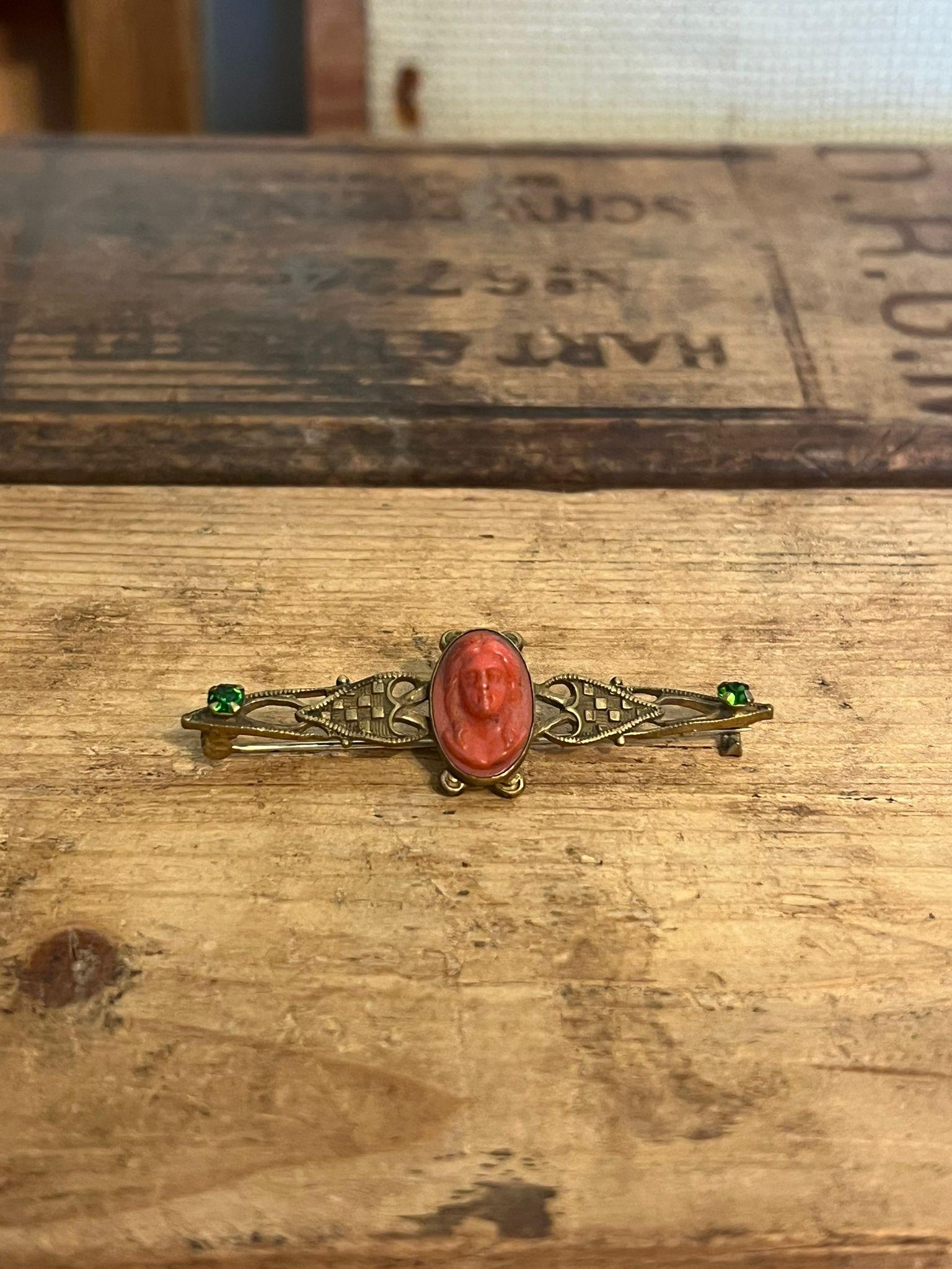   Possibly Coral on brass, materials unconfirmed. Bar Pin Art Deco with small (unknown) green jewels. Vintage condition as pictured. Listing is for described item only.Box H2

Dimensions. 2.25” W ; 1” D ; 0.50 H