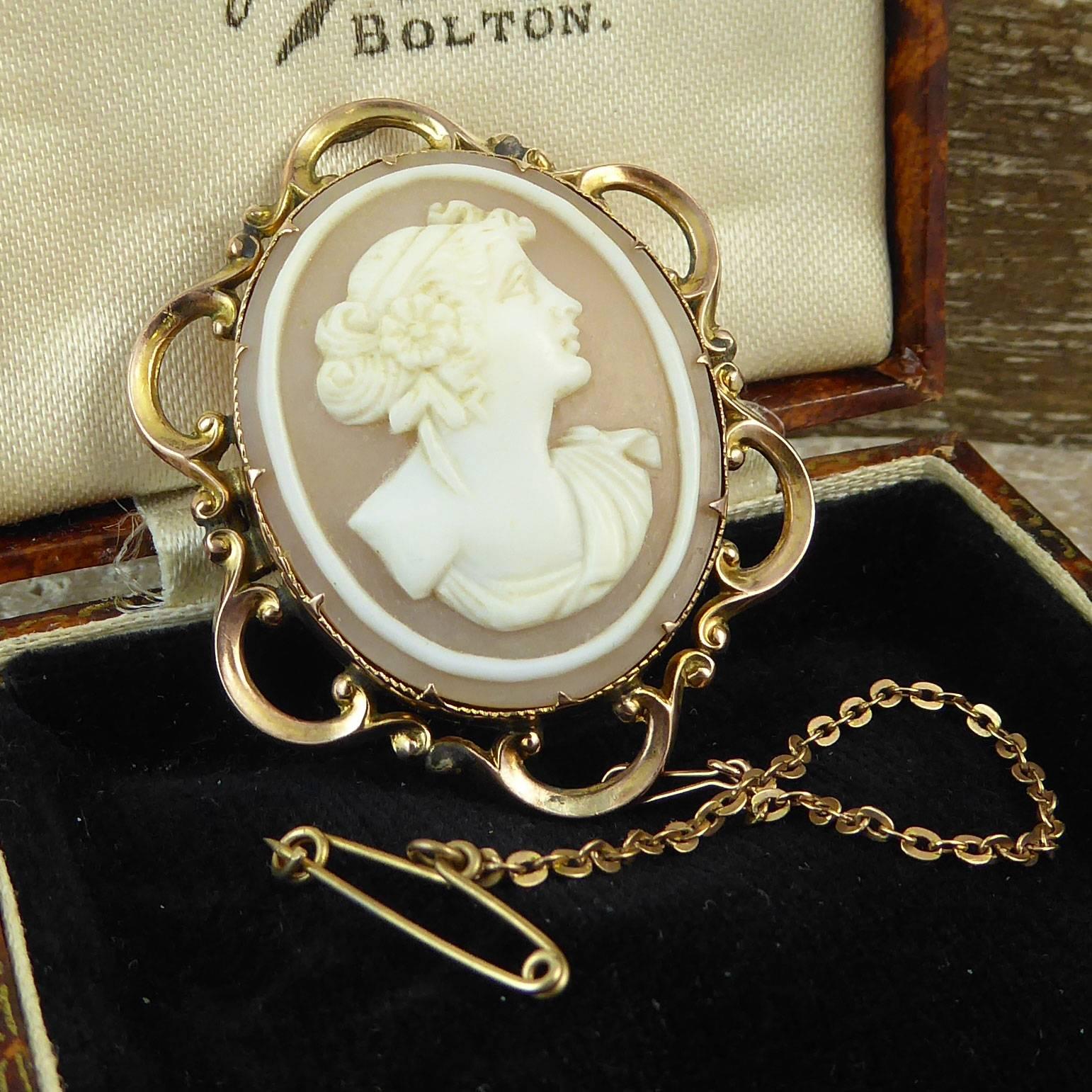 A Victorian oval cameo beautifully carved in shell and depicting a woman in profile.  With classical styling showing an upswept hairstyle with floral decoration and a the folded fabric of a necklace gathered to one shoulder.  The shell has been