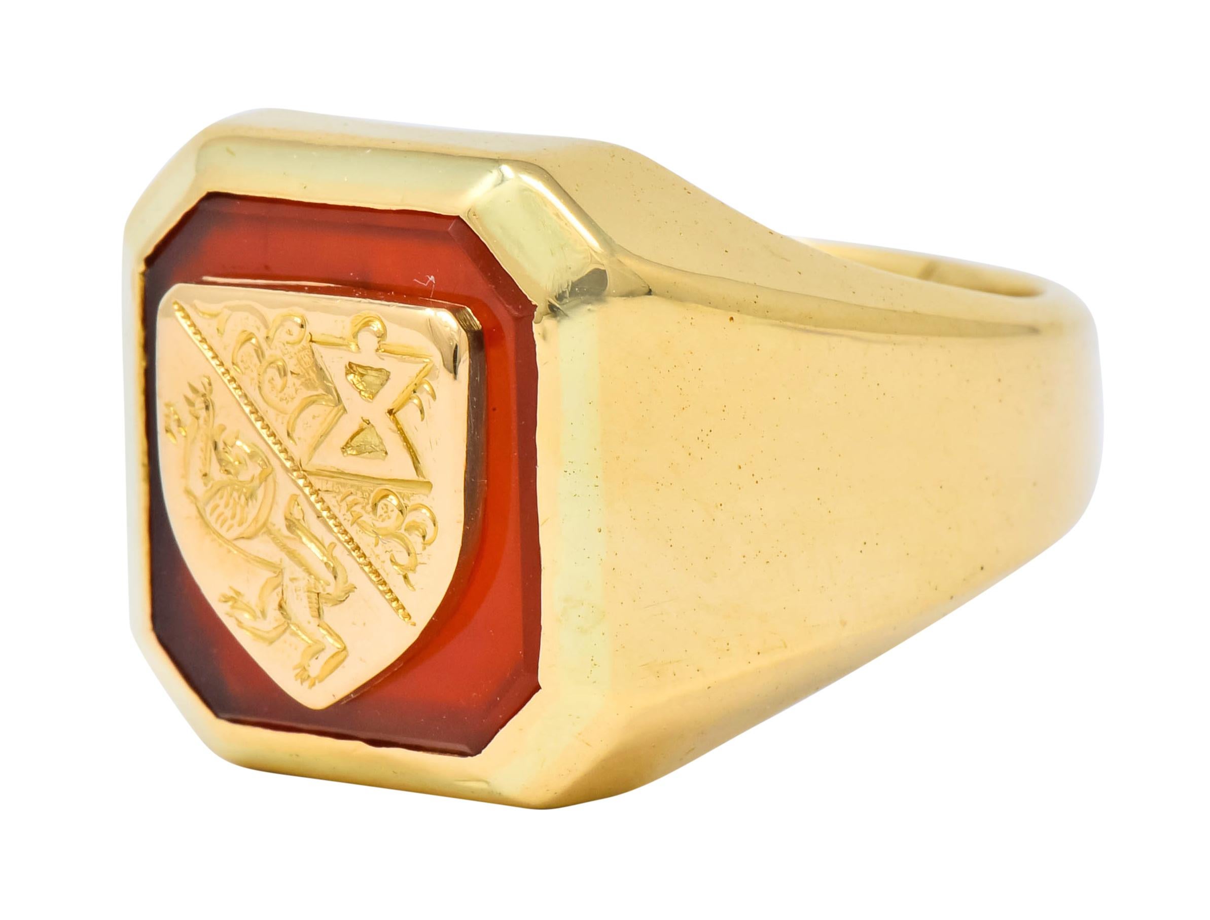 Signet style ring with bezel set square cut carnelian tablet measuring approximately 9/16 x 9/16 inch, translucent and reddish-orange in color

Carnelian centers a raised yellow gold shield, bisected diagonally depicting a roaring lion and hour