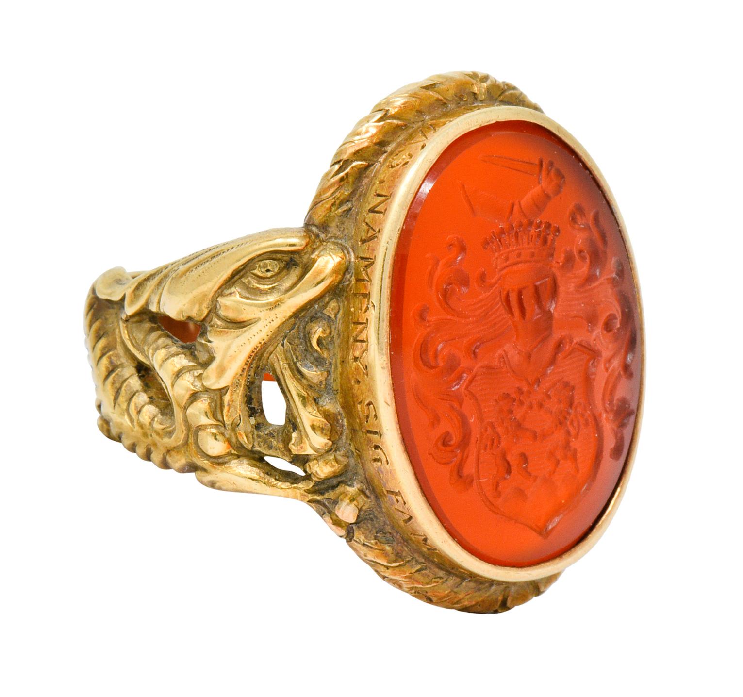 Centering an oval carnelian intaglio, translucent rust red in color, set in a deeply inscribed bezel

Depicts a crowned knight and shield that is emblazoned by two dueling lions with swirled foliate; all topped by a flexed arm grasping a
