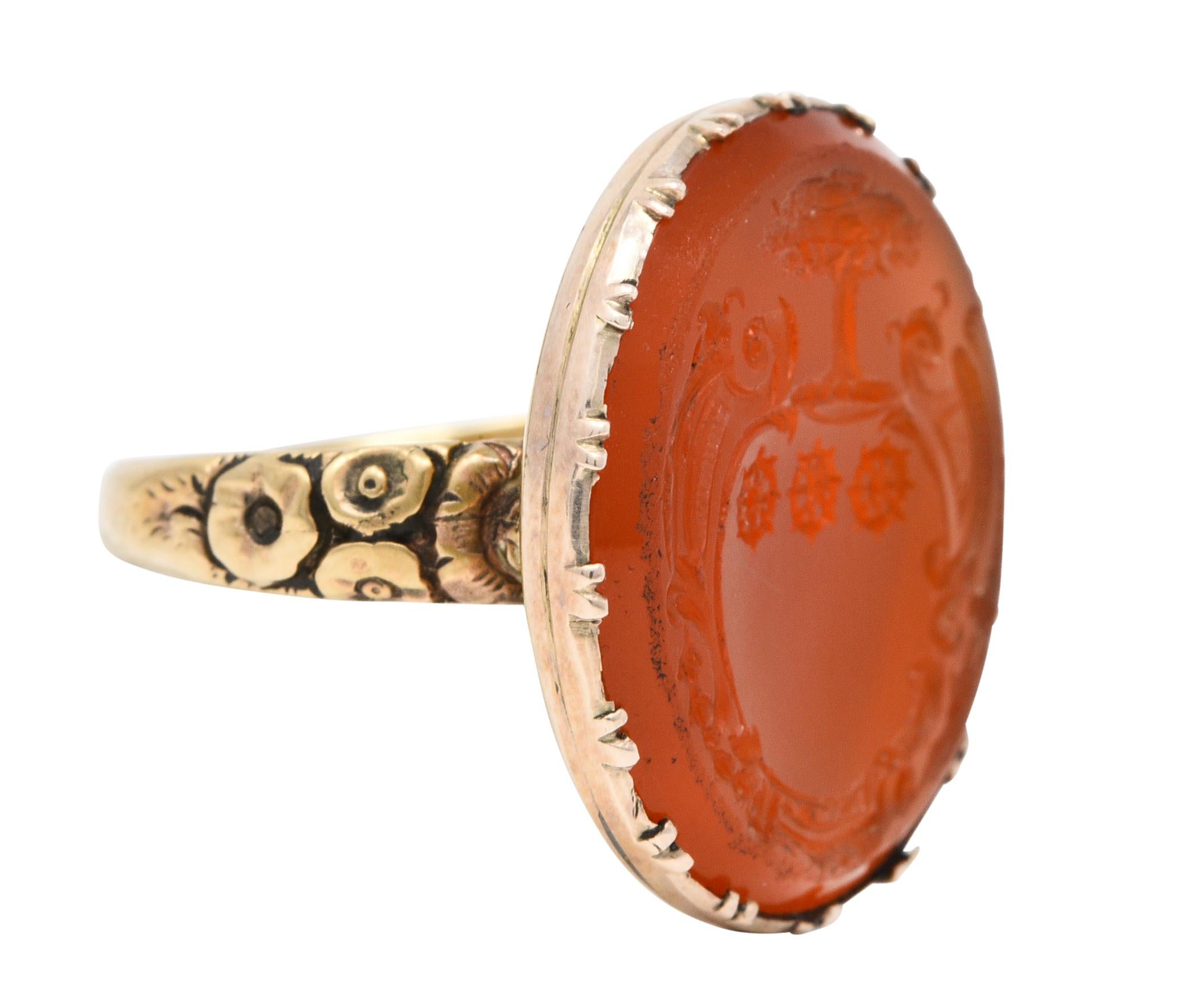 Featuring a carved oval carnelian measuring approximately 21.0 x 19.0 mm

Vibrantly translucent orange and uniform in color

Depicting a whiplashed cartouche shield with three spoked wheels topped by a flourishing tree

Tree is symbolic of strength
