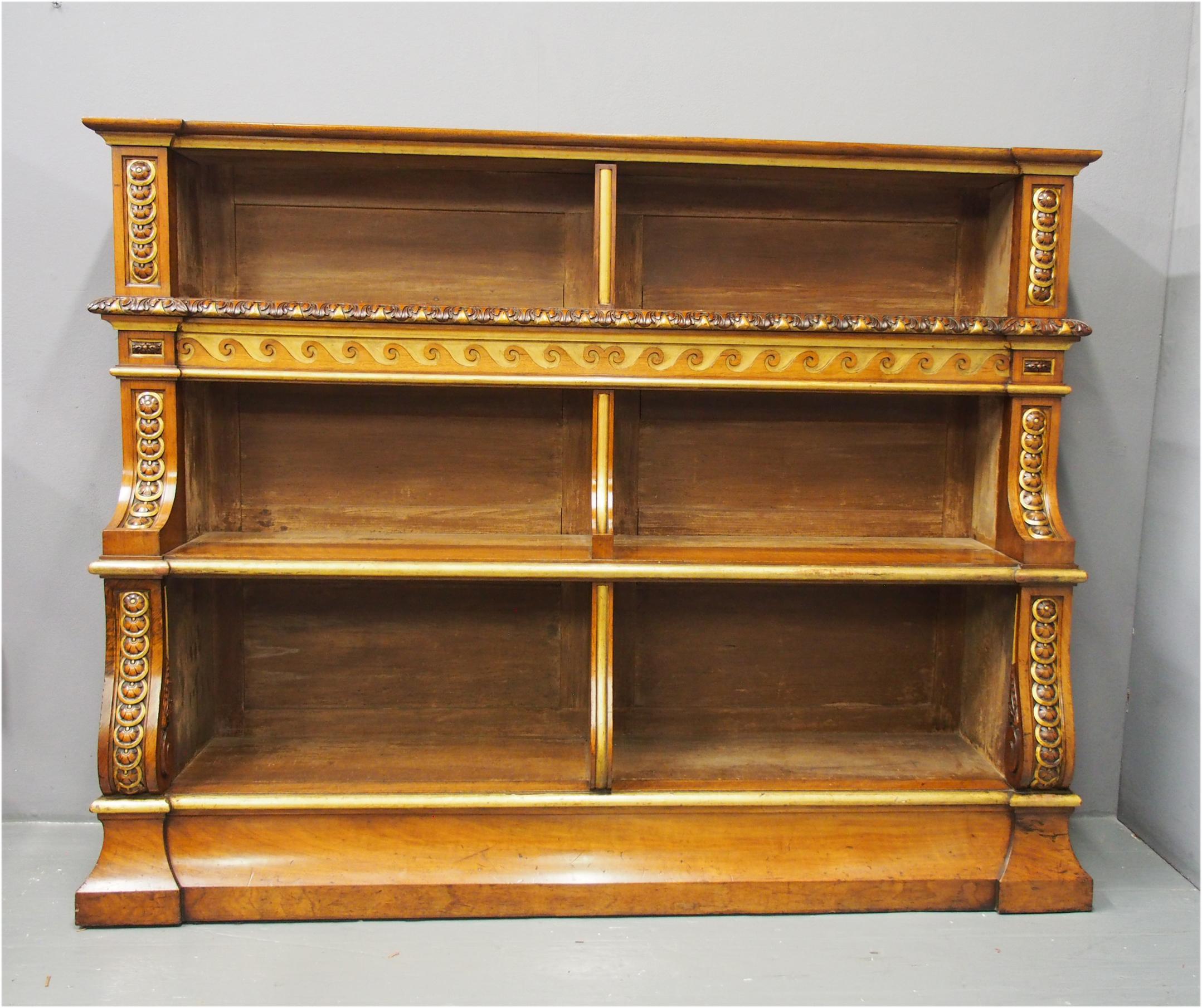 Mid Victorian carved and gilded walnut waterfall bookcase, circa 1850. With solid walnut top and the 3 shelves are divided into 2 sections. Flanked by pilasters carved with rondels and flower heads featuring gilded bezels. The top shelf has a