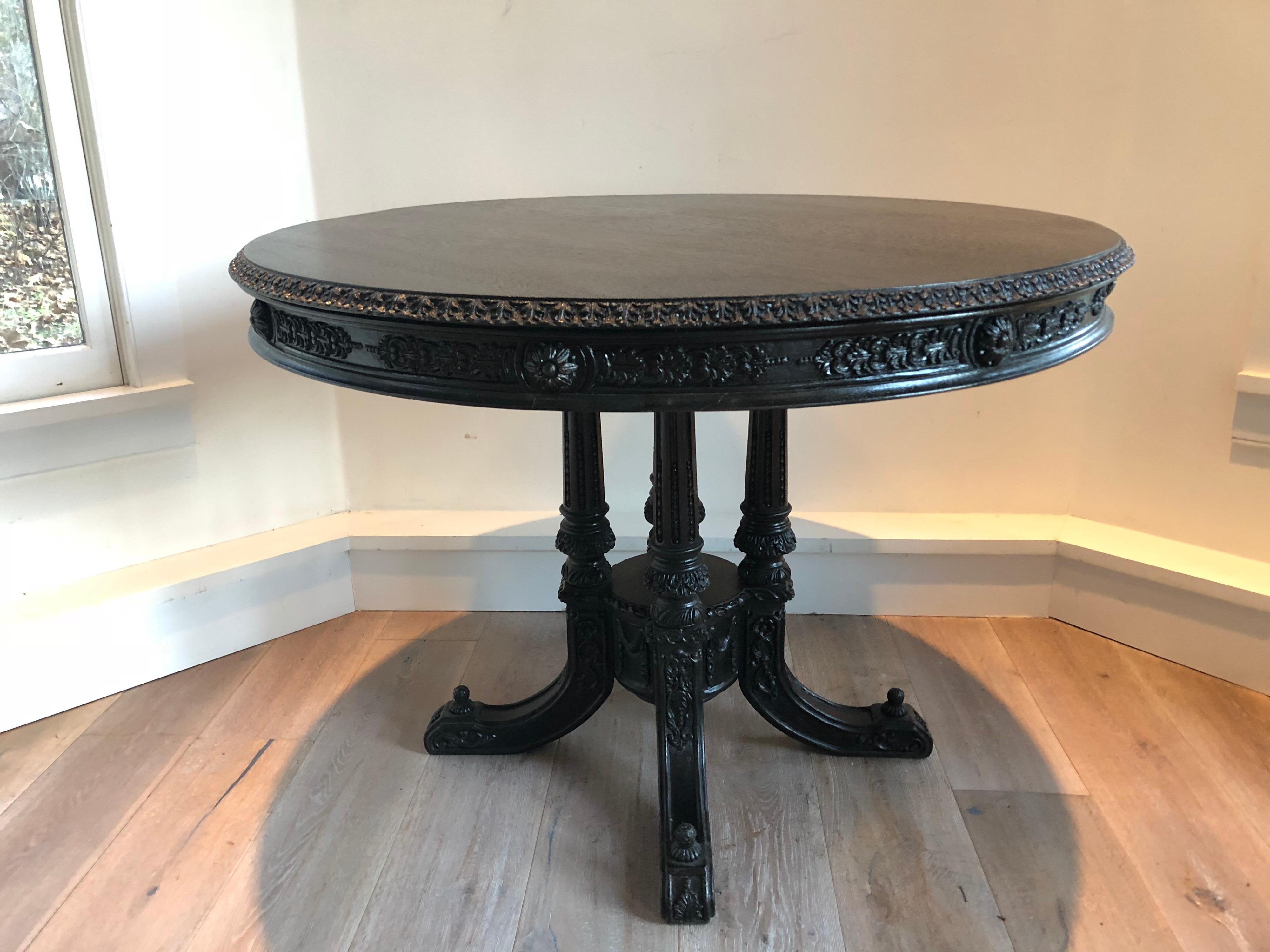 A Victorian carved center table with ebonized finish. Intricately carved pedestal base and surround.