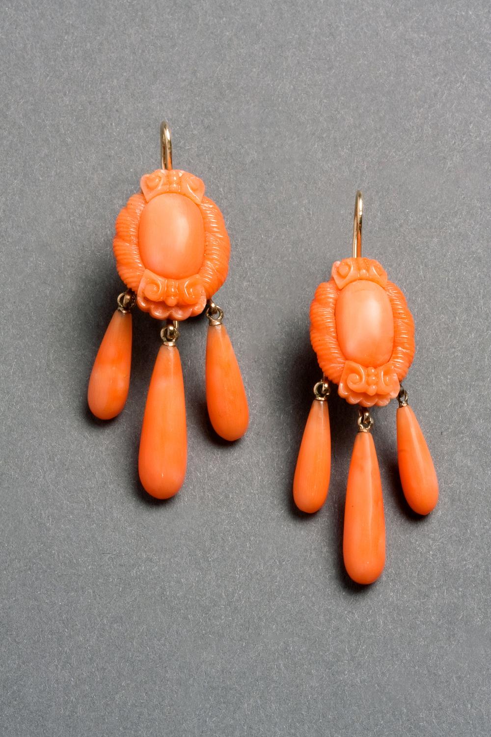 A delightful pair of coral ear pendants from the mid-Victorian era in wonderful original condition, each designed as a polished oval dome surrounded by carved floral motifs and twisted ropework borders in a pale orange-pink coral. Discreet rose gold