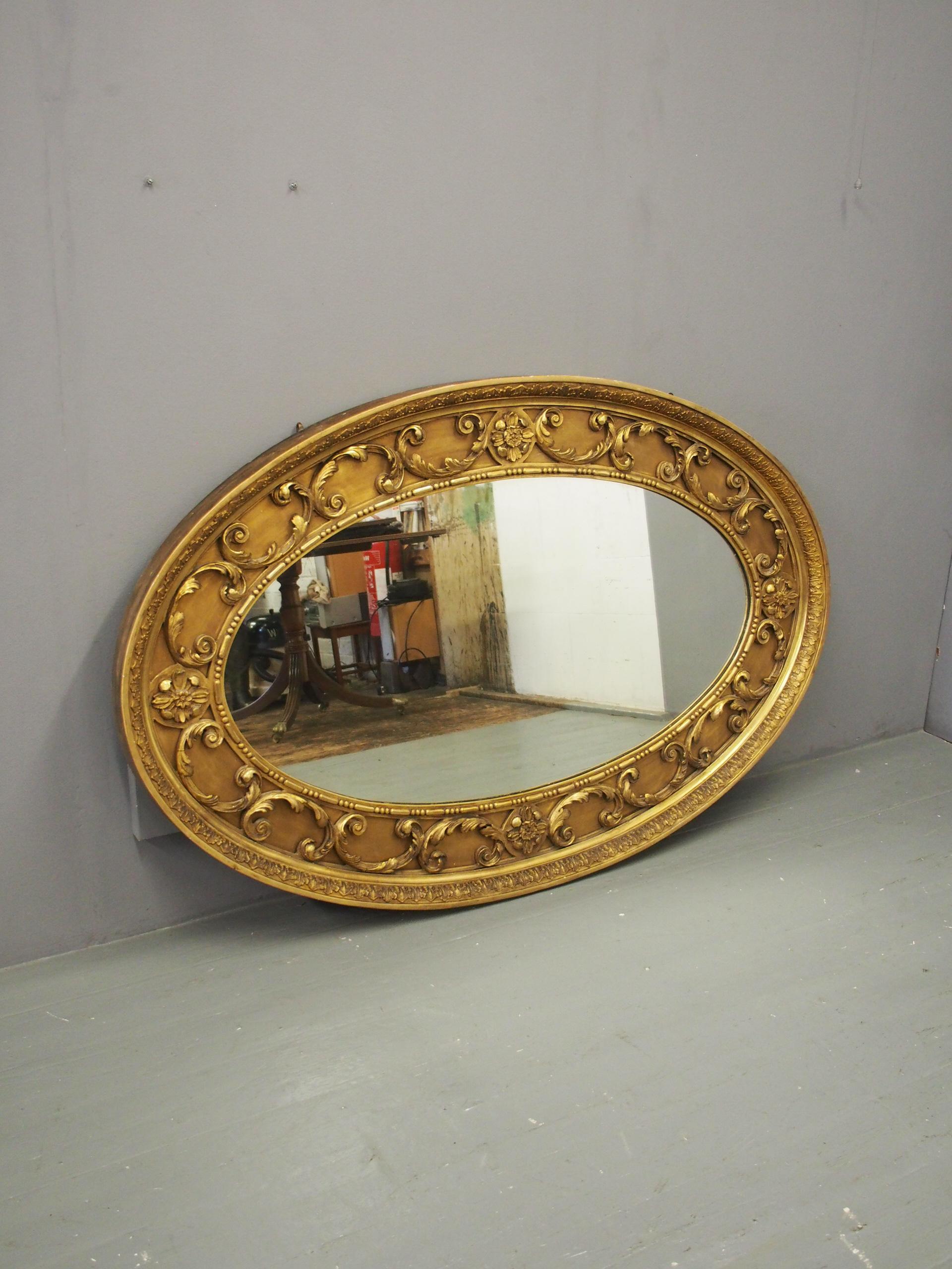 Victorian carved giltwood and gesso oval mirror, circa 1860. The giltwood frame has a foliate gesso pattern to the outside with carved, gilded C-scrolls intersected by large flower heads. Inside is an egg and dart carved, gilded border with its