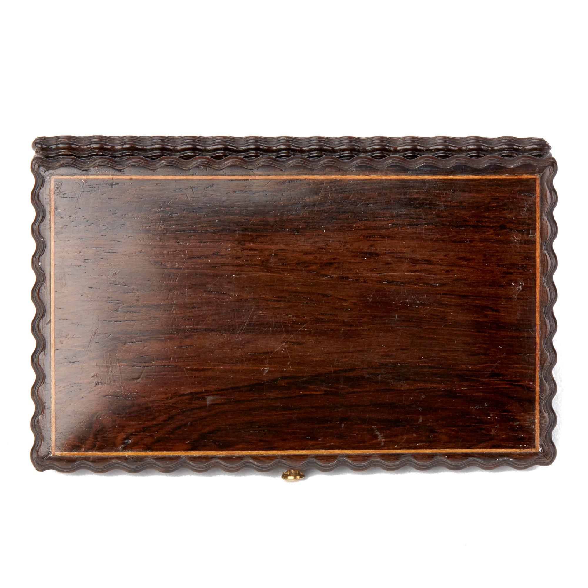 A very fine antique carved rose wood needle case with hinged cover with spring clasp and with central inset brass cartouche, the edges of the box with finely carved detail and with inset contrasting wood piping around the edges of the top and base