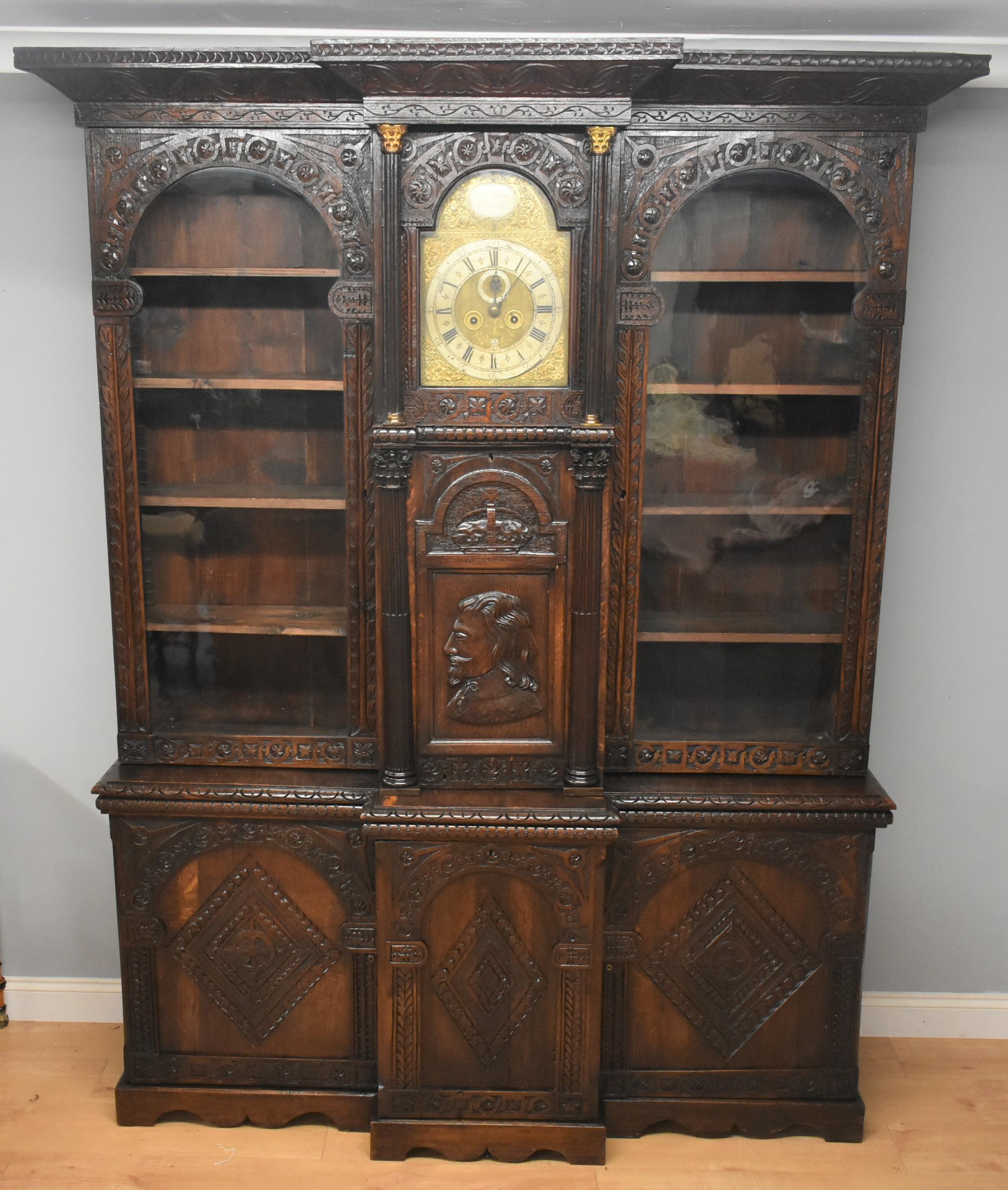 Victorian hand carved oak breakfront display cabinet or bookcase, it has a nicely carved cornice with centre section housing a brass dial clock by Phil Walton Devizes. Phil Walton was an apprentice to a London clock maker in 1707 and then went on to