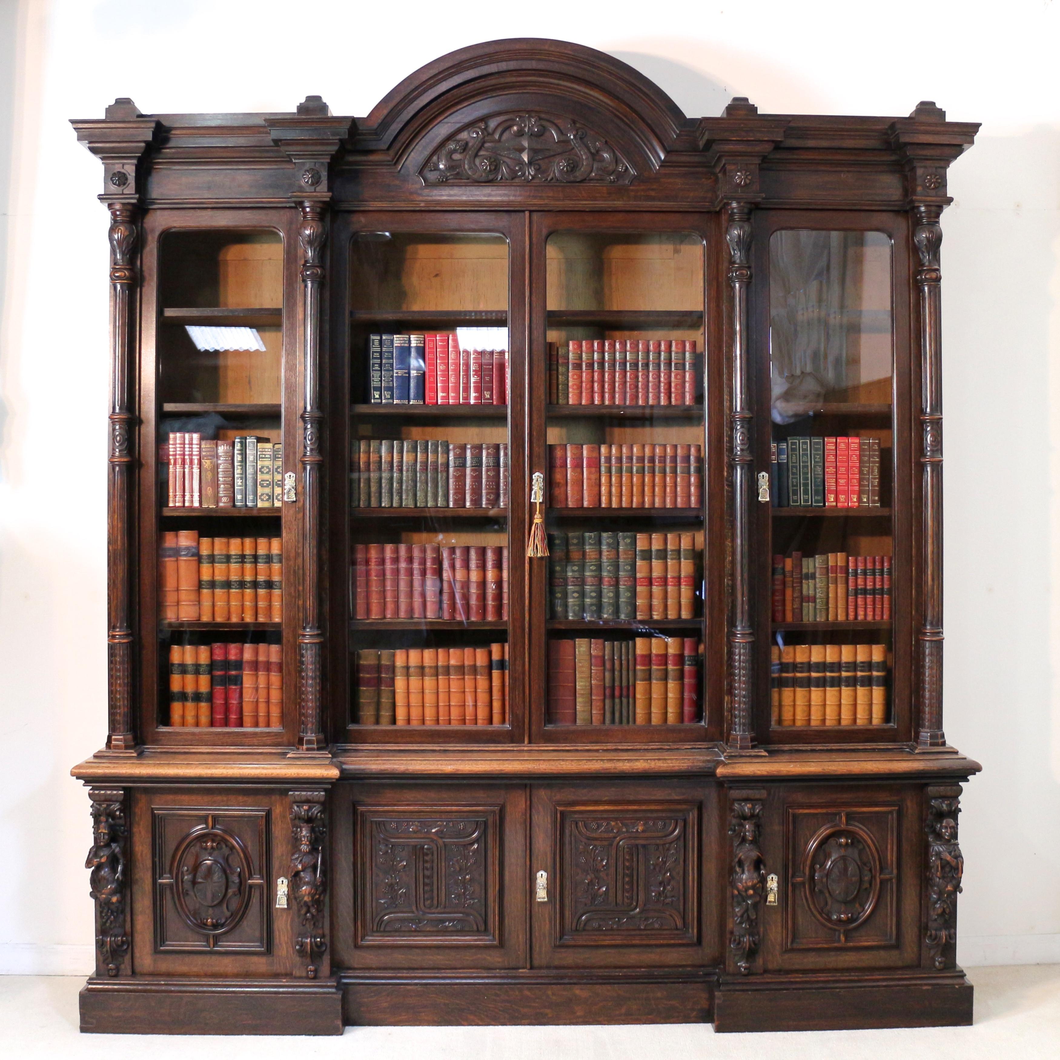 A magnificent Victorian carved oak Elizabethan Revival four door inverted breakfront bookcase dating to circa 1880. With slightly domed square finals to the pediment and a moulded domed cornice carved with dragons it has four rounded glazed doors