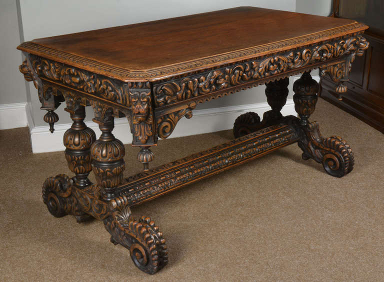 Victorian carved oak library or center table the rectangular top with molded edge and canted corners above a fluted and mask-carved shaped frieze hung to the corners with fluted pendant finials and with boss-applied cusp-carved lower edge, with