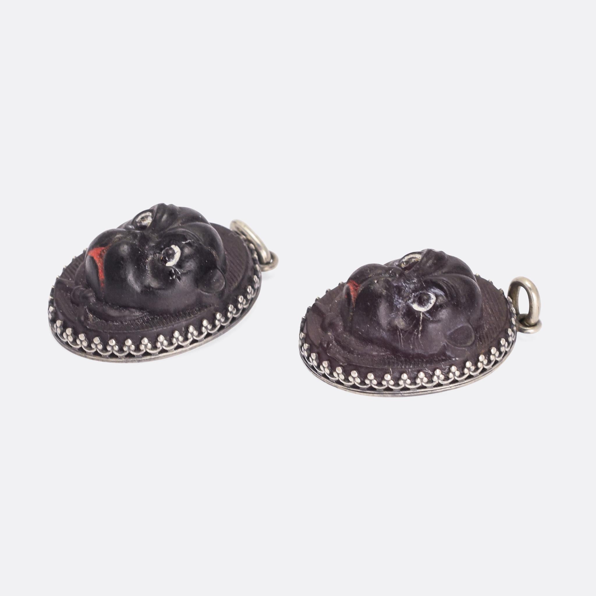 An incredible Victorian carved glass pug pendant mounted in silver . It has painted eyes and mouth and a bow tied under the chin; it's made of deep purple coloured glass. The mount features Etruscan-style embellishment, and it dates from the latter