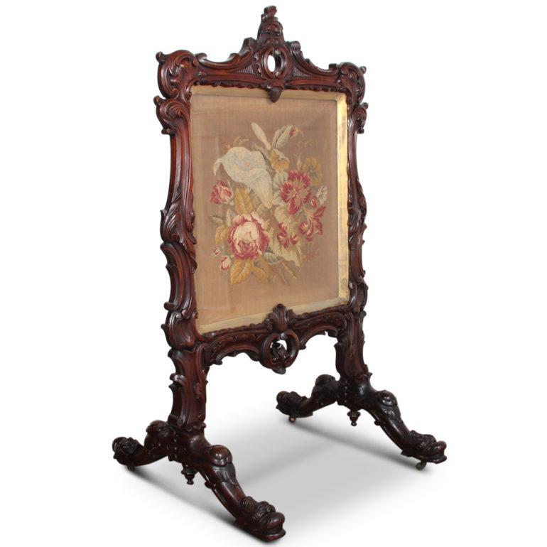 An elaborately carved, solid rosewood, Victorian Rococo-style summer screen, the frame with carved flowers and leafs, the base carved in the manner of four dolphins. Needle-point floral still-life scene under glass.



  