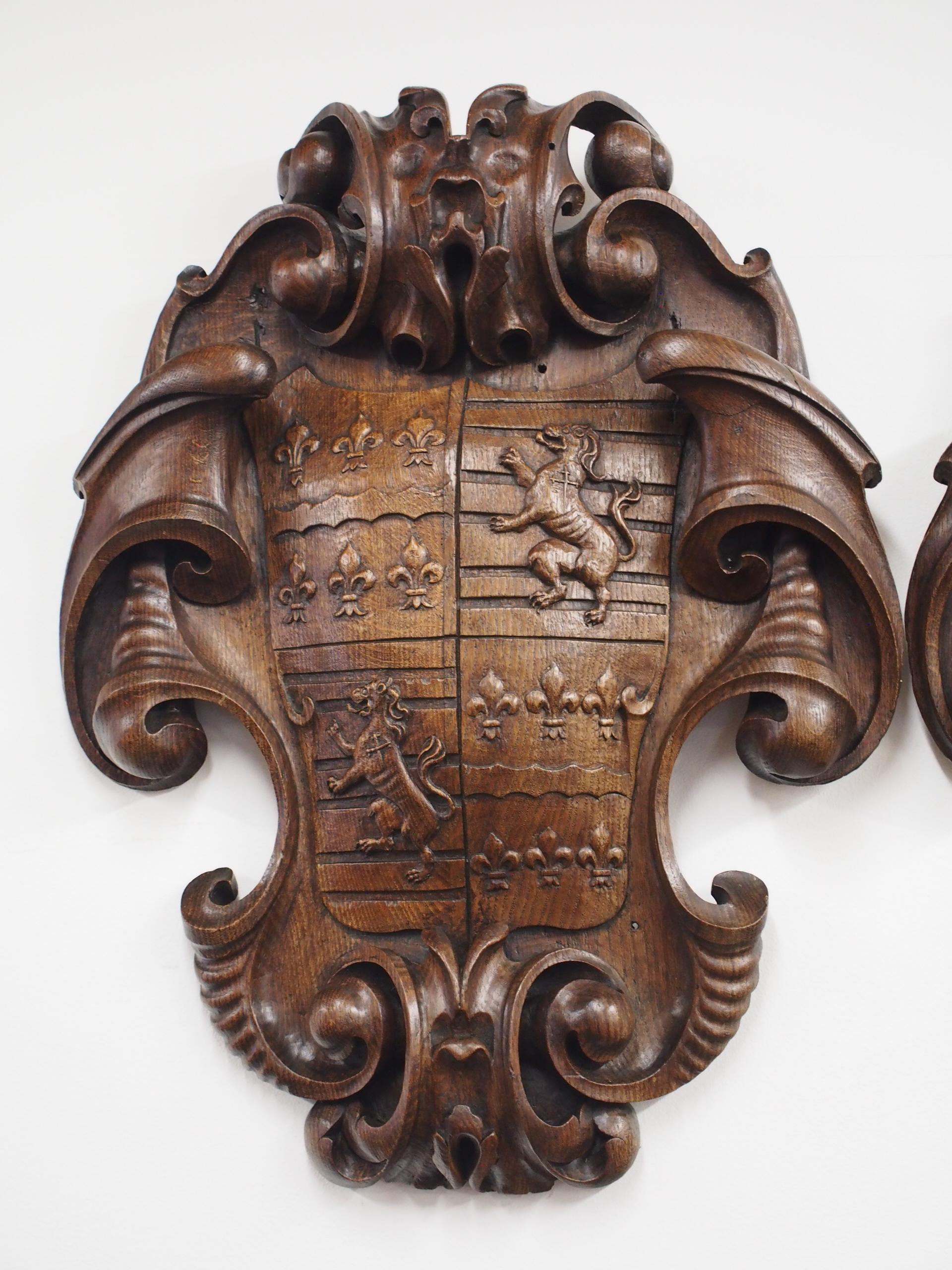 Pair of profusely carved shield plaques, circa 1860. With rococo styling to the top and paper fold designs, the centre is bombe-shaped and is carved with the fleur-de-lis and lion rampant. The other plaque has a similar shape but the centre has a