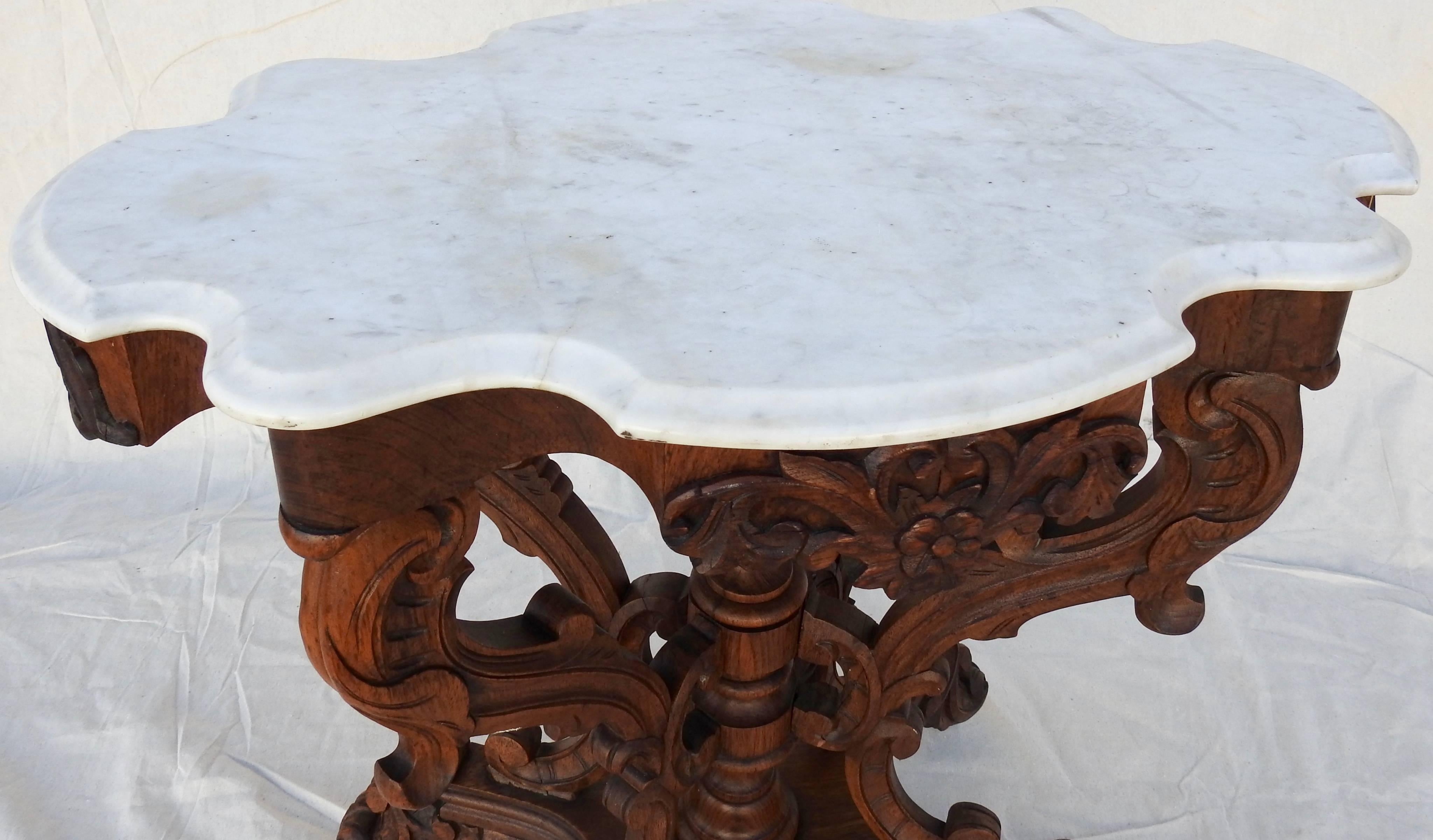 Offering this exquisite carved walnut Victorian marble-top table. A large hand carved finial in the center of the base is surrounded by lots of hand carved scrollwork and foliate details that make the pedestal and legs. The sides of the table have a