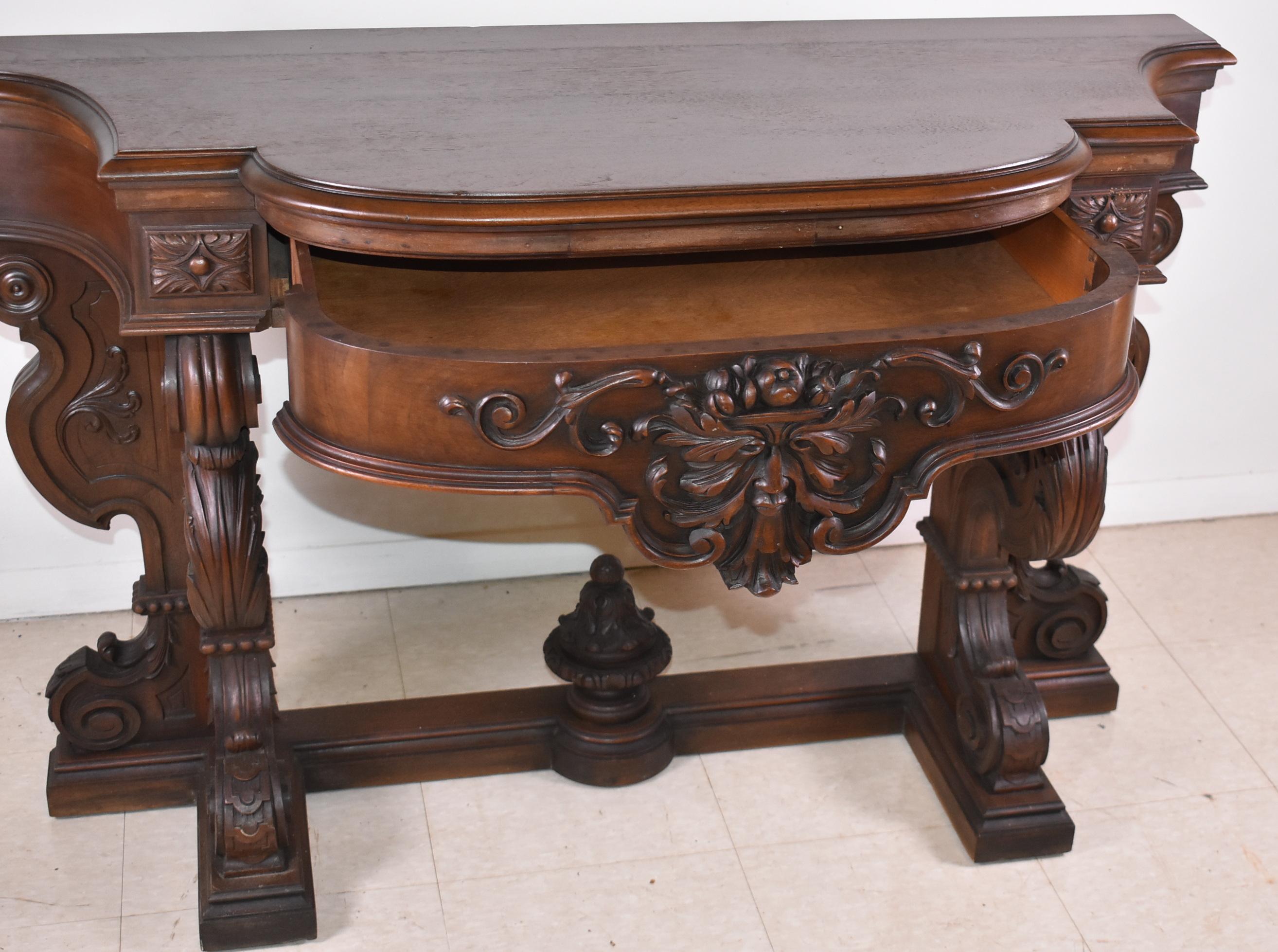 Victorian walnut console table circa 1890's with a carved face in the center and additional detail on the base with a central drawer. 48