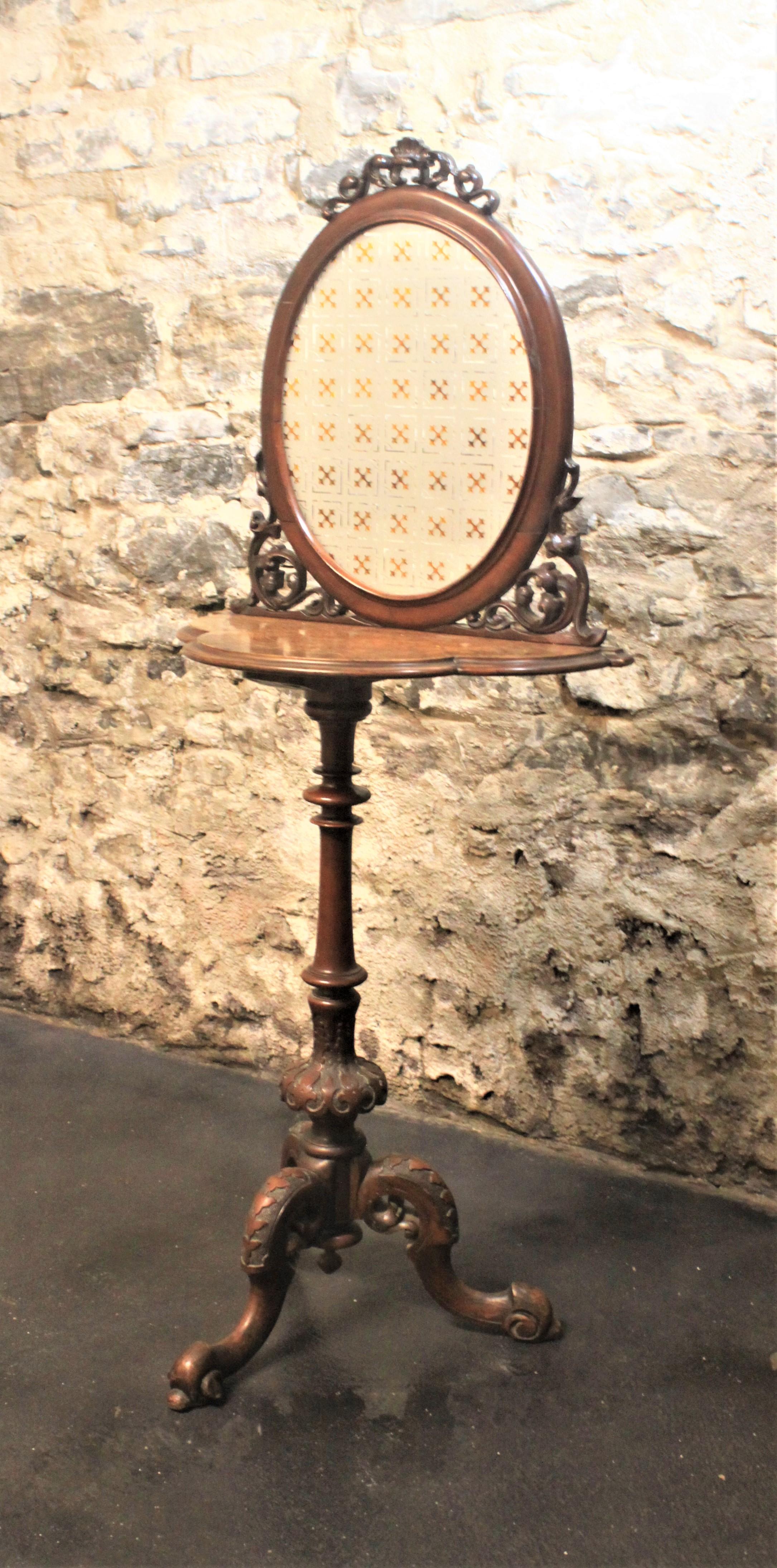 Dating from the Victorian period and likely being made in England is a unique and decorative demilune style accent table or candle stand. The pedestal legs and upper frame are carved walnut and the tabletop is inlaid with a decorative design. The