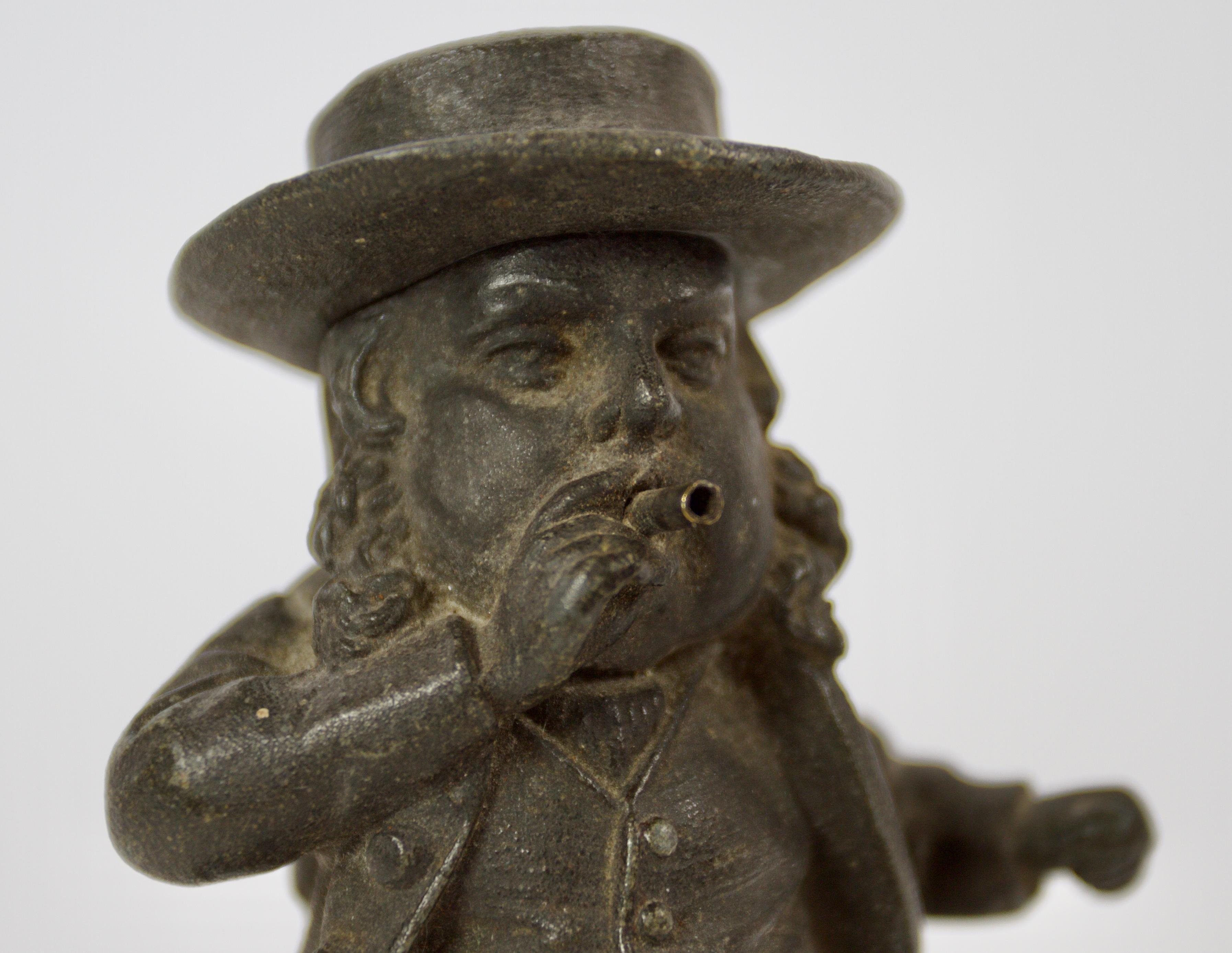 Victorian Cast Iron Bar/counter Cigarette Lighter
In the Form of a smoking Gentleman. 
Hat Hinges open, the hollow body to hold a coil wick
with threads through the gentlemans mouth 
Which would be  alight with a flame
Circlular base with wording A