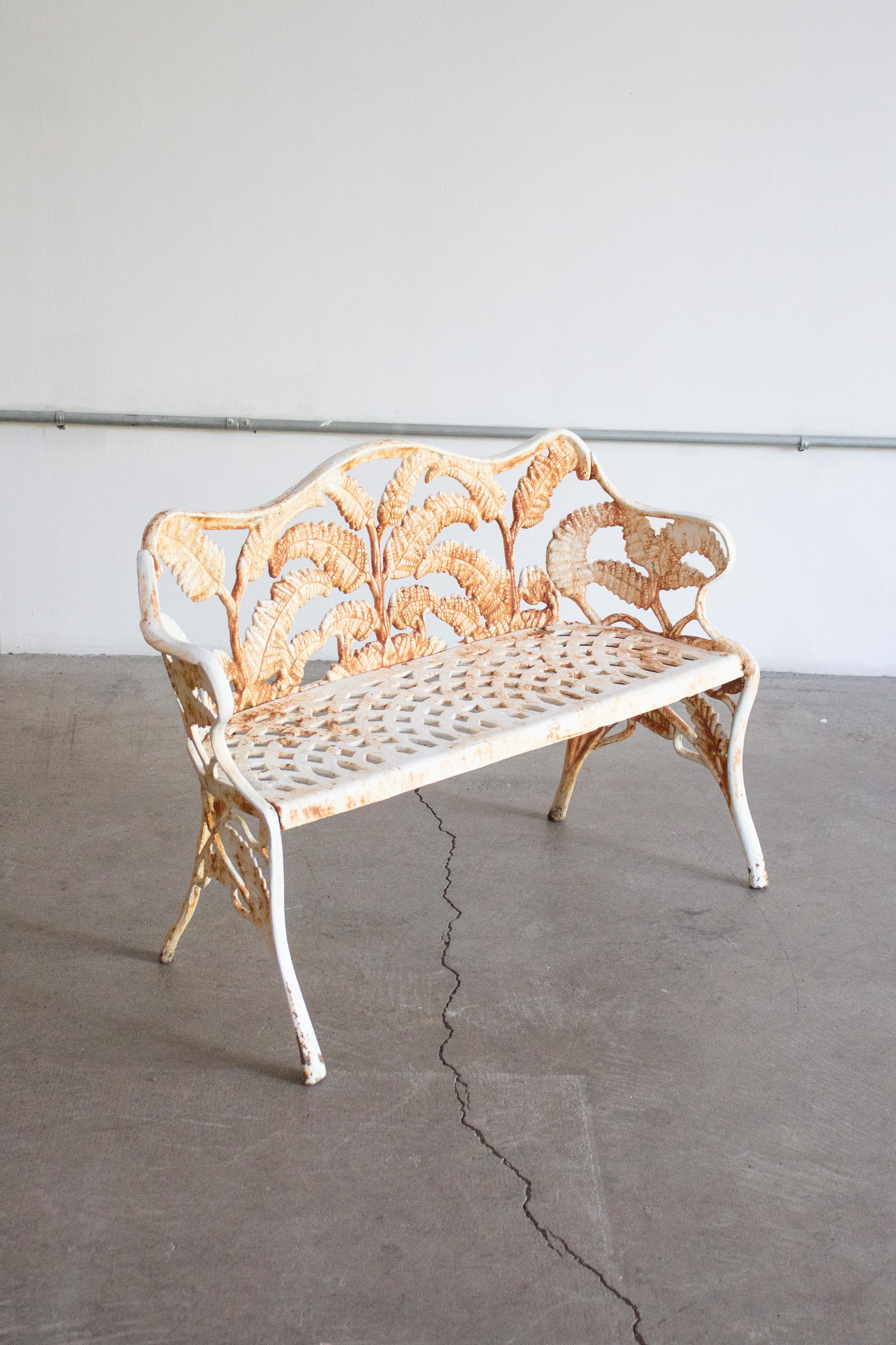 A petite Victorian cast iron garden bench in a “Fern” pattern. White paint with areas of rust showing though. Substantial heavy weight. Pair of chairs also available, sold separately.